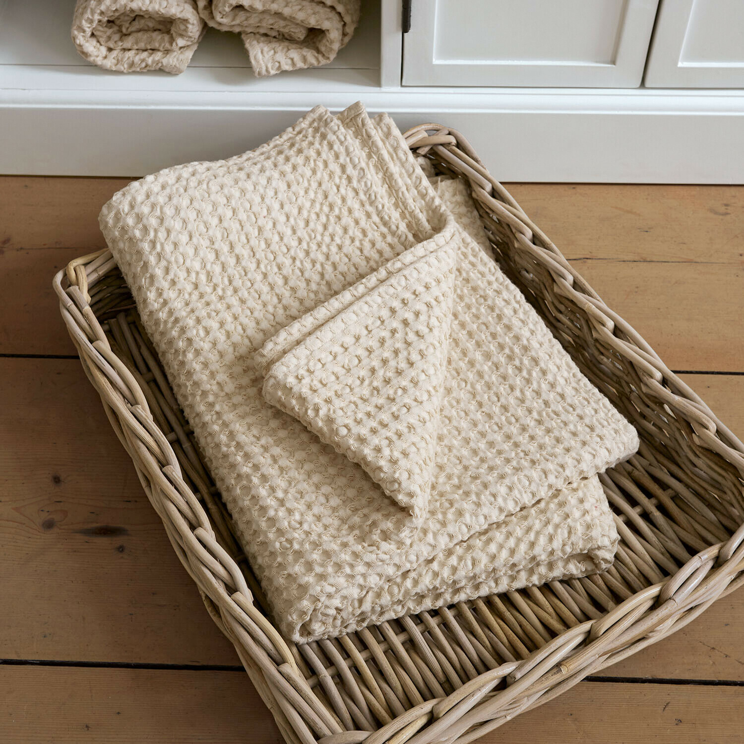 Telo doccia Maralei Coperta crema in cotone con trama a nido d'ape in cesto di vimini su pavimento in legno