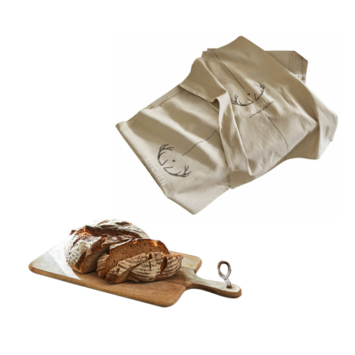 Tovaglia beige in lino con motivo corna di cervo accanto a tagliere in legno con pane