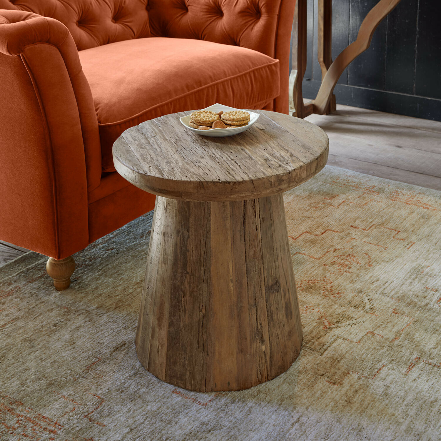 Tavolino di complemento Yarwood Tavolino in legno naturale davanti a un divano arancione e tappeto con motivo discreto