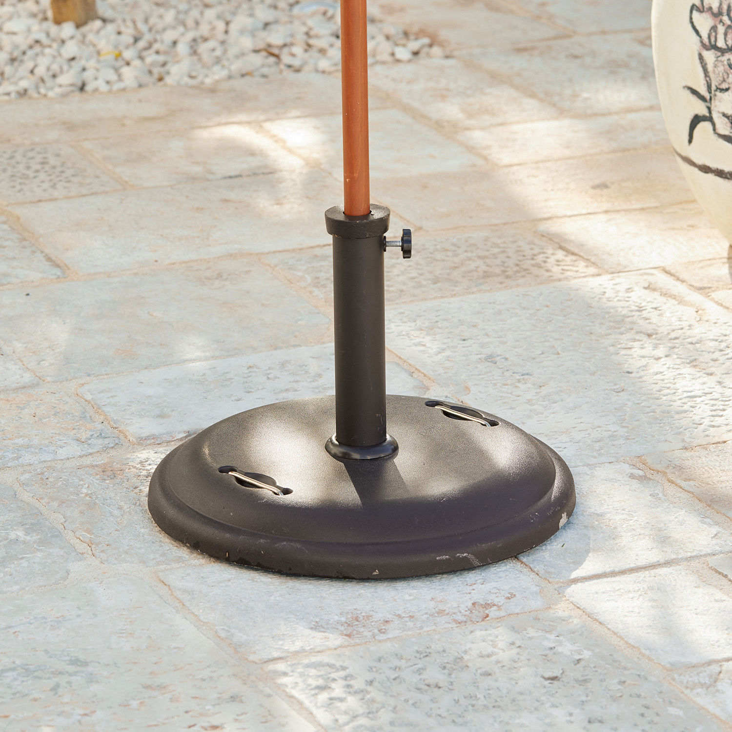 Base per ombrellone Yarra Base per ombrellone in metallo nero su pavimento in pietra per giardino o terrazza