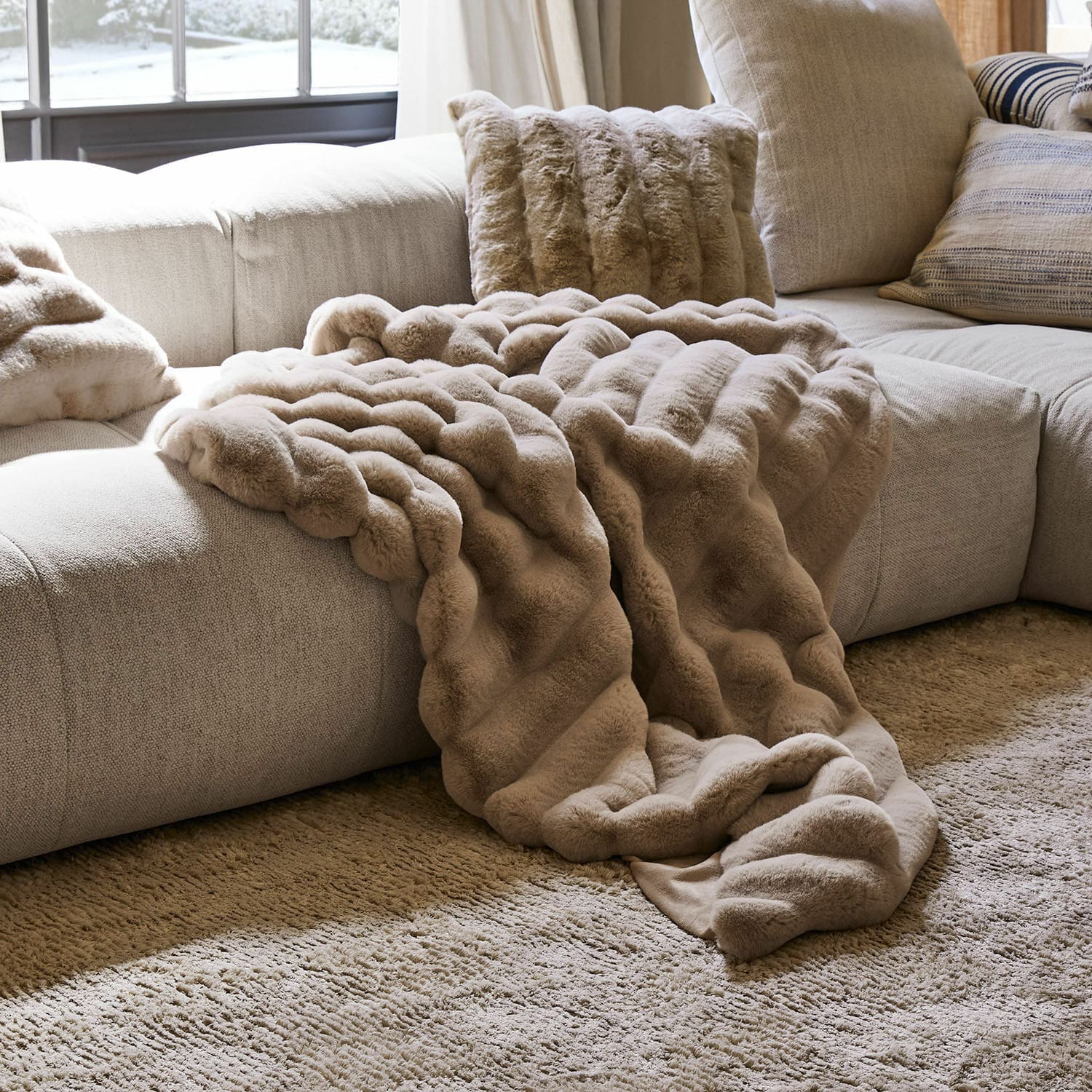 Coperta e cuscino in pelliccia sintetica beige su divano grigio chiaro in soggiorno accogliente