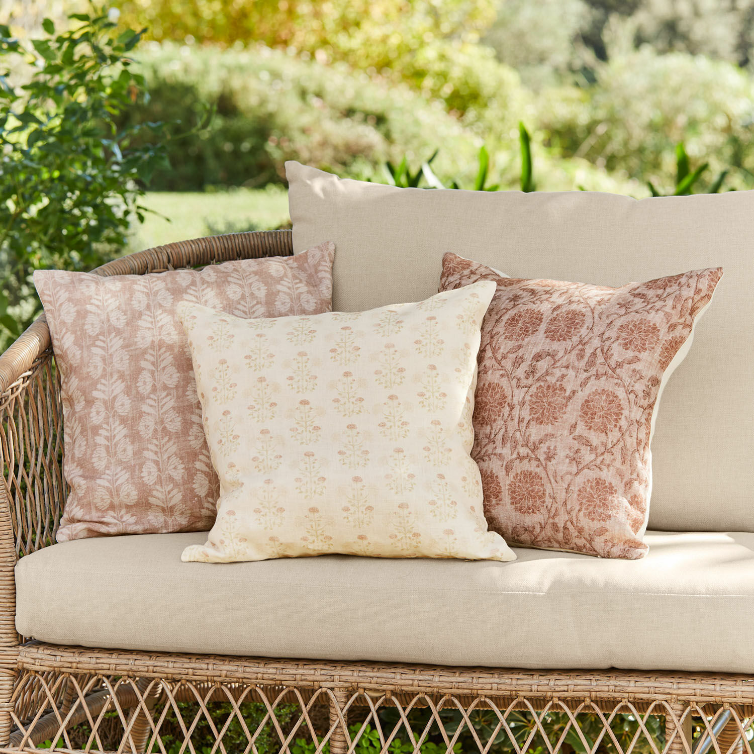 Set di 3 copricuscini Tarouja Set di tre cuscini decorativi in cotone beige e rosa su divano in vimini da giardino