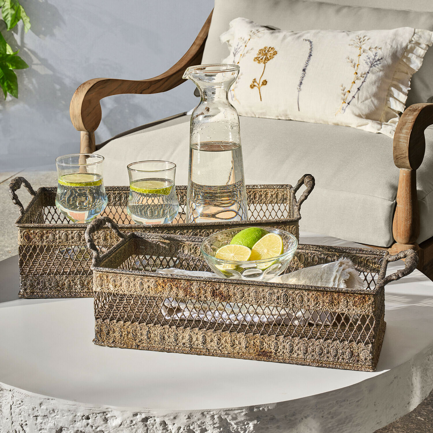 Due vassoi in metallo rustico con manici su tavolo bianco con caraffa e bicchieri d'acqua al lime
