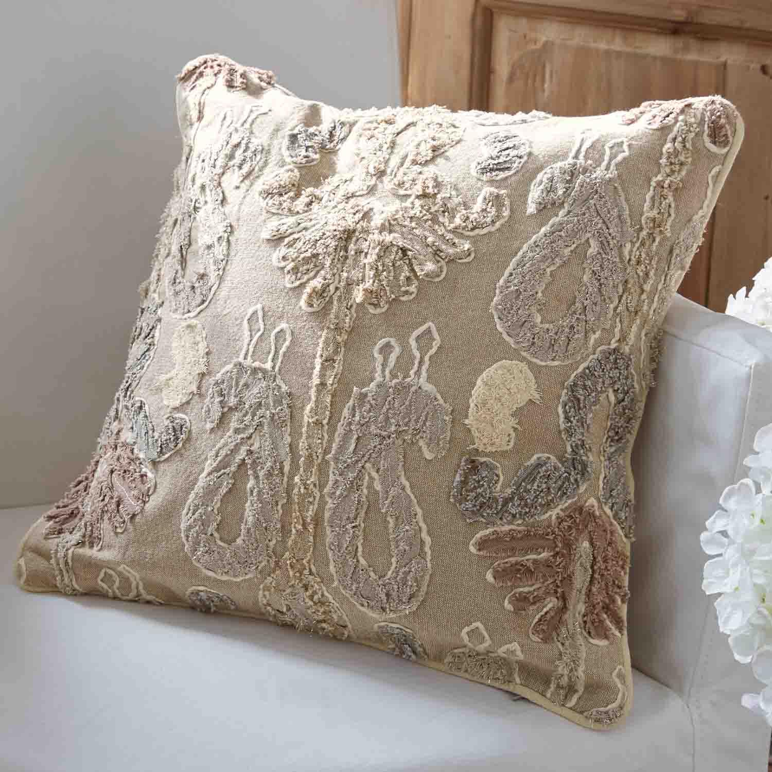 Cuscino decorativo beige con motivo ricamato in colori pastello su divano bianco