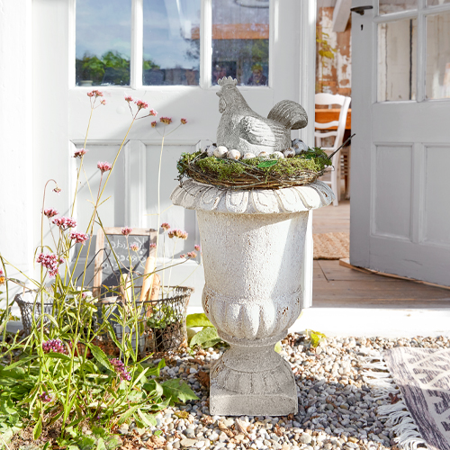 Vaso decorativo bianco in pietra con figura di gallina e nido con uova all'esterno vicino alla porta