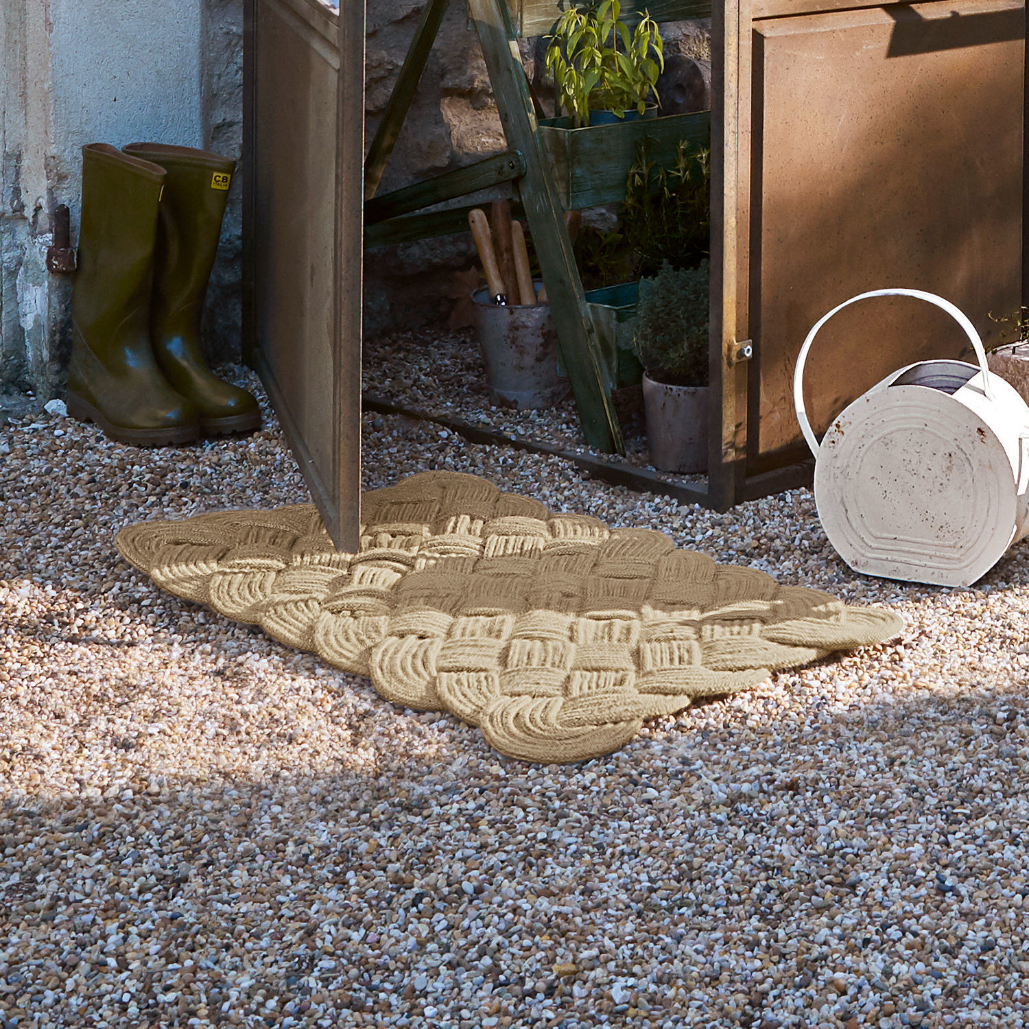 Stuoino Harman Zerbino beige intrecciato in materiale naturale su ghiaia davanti a porta da giardino aperta