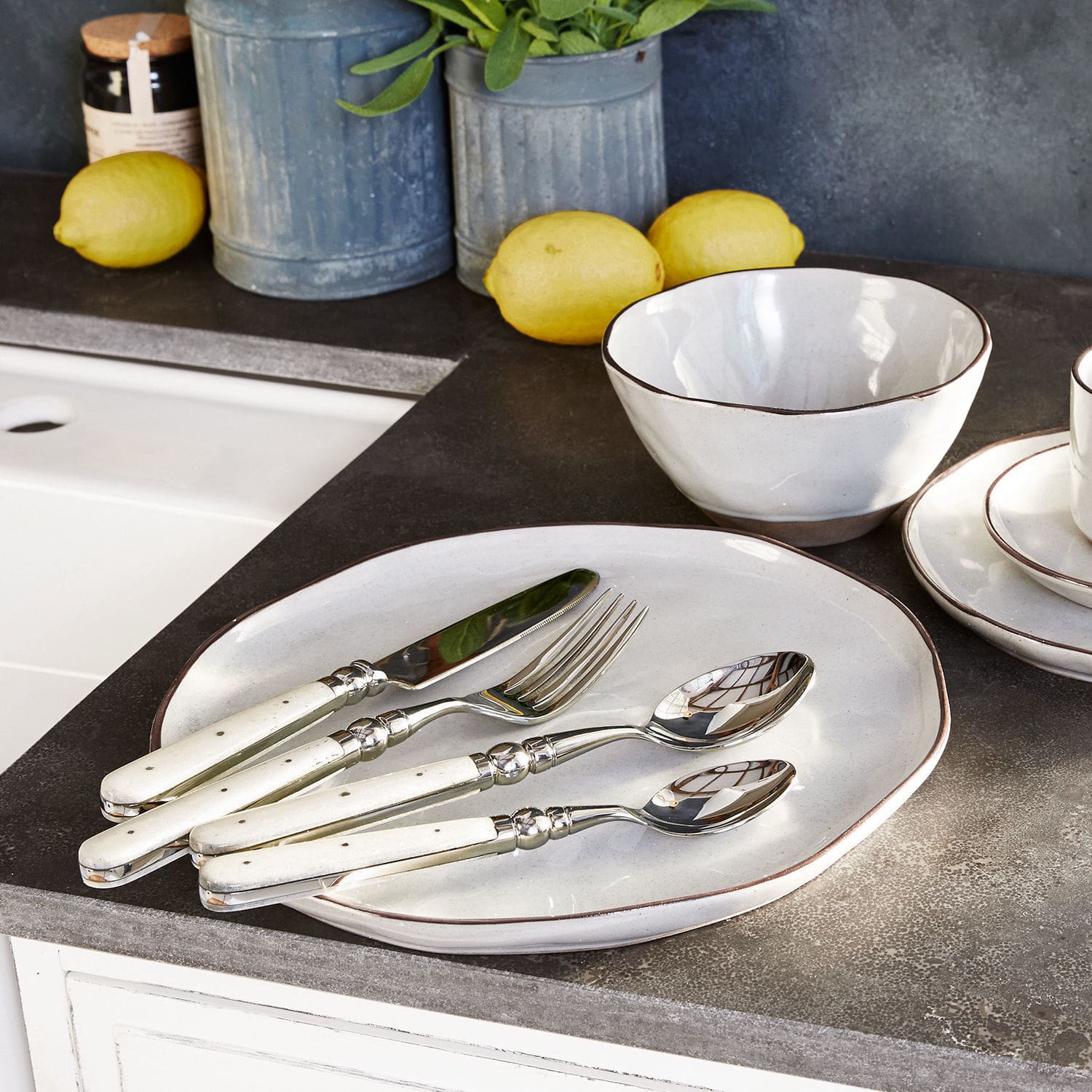 Set di 6 piatti Biarré Set di posate con manico bianco su piatto e ciotola in ceramica su piano cucina con limoni