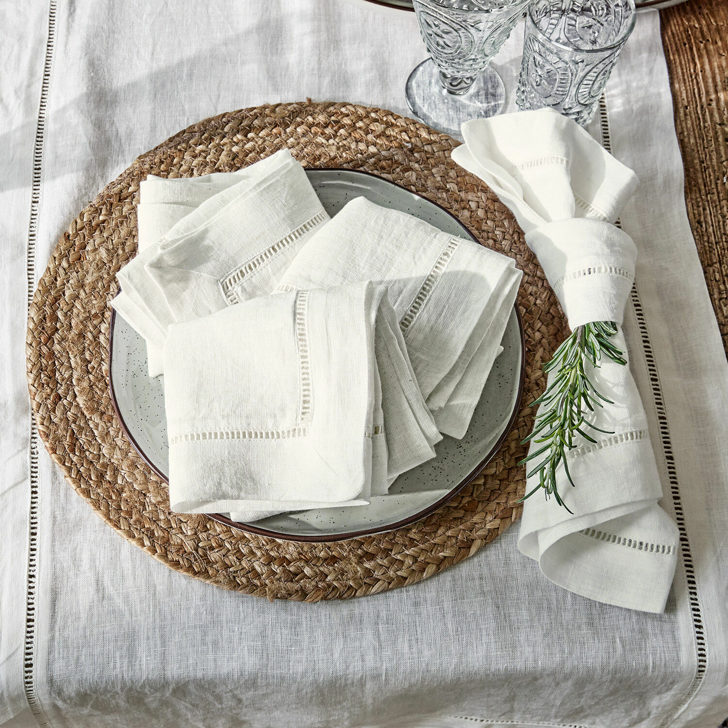 Set di 4 tovaglioli Covent Garden Tovaglioli di lino crema su piatto con sottopentola intrecciato e decorazione di rosmarino