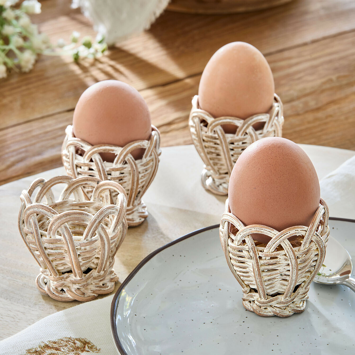 Set di 4 portauova in rattan Minouvelle Set di quattro portauova in vimini bianco invecchiato su tavolo in legno, stile rustico