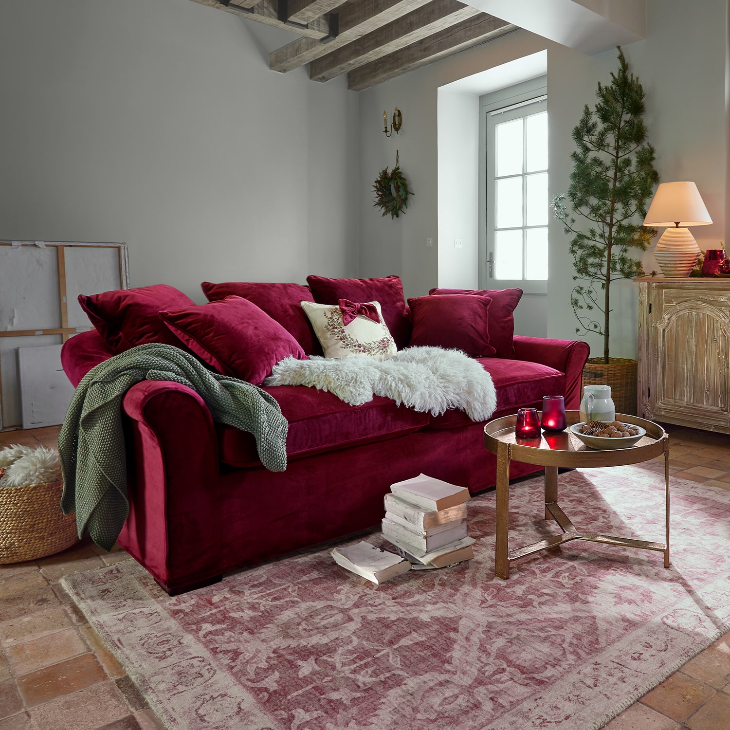 Divano rosso in velluto con cuscini e coperta morbida in soggiorno accogliente con scala in legno