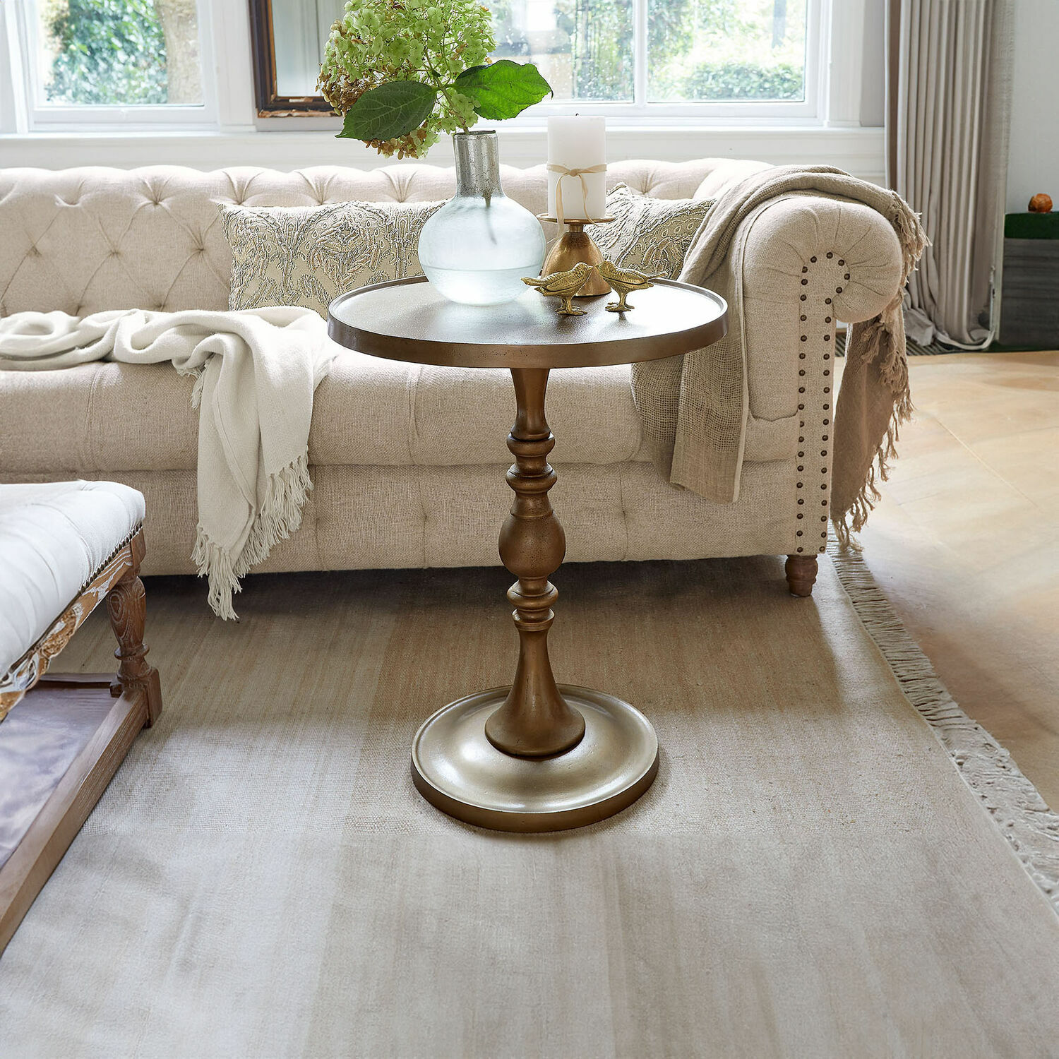 Tavolino di complemento Uralive Tavolino rotondo in metallo color ottone davanti a divano beige con decorazioni in soggiorno