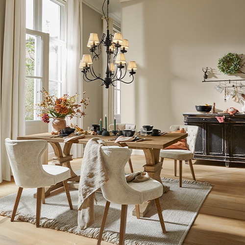 Sala da pranzo con tavolo in legno, sedie imbottite crema, decorazioni floreali e lampadario nero
