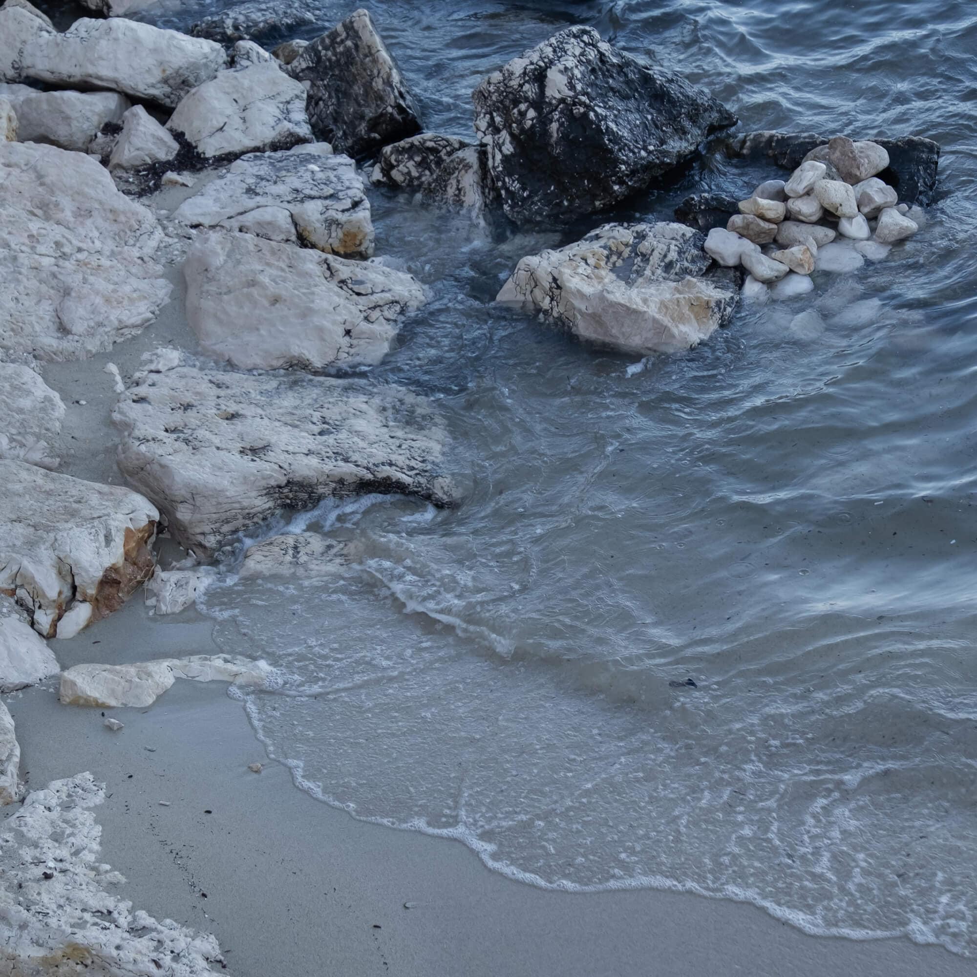 Riva con rocce chiare e scure e onde che si infrangono sulla sabbia