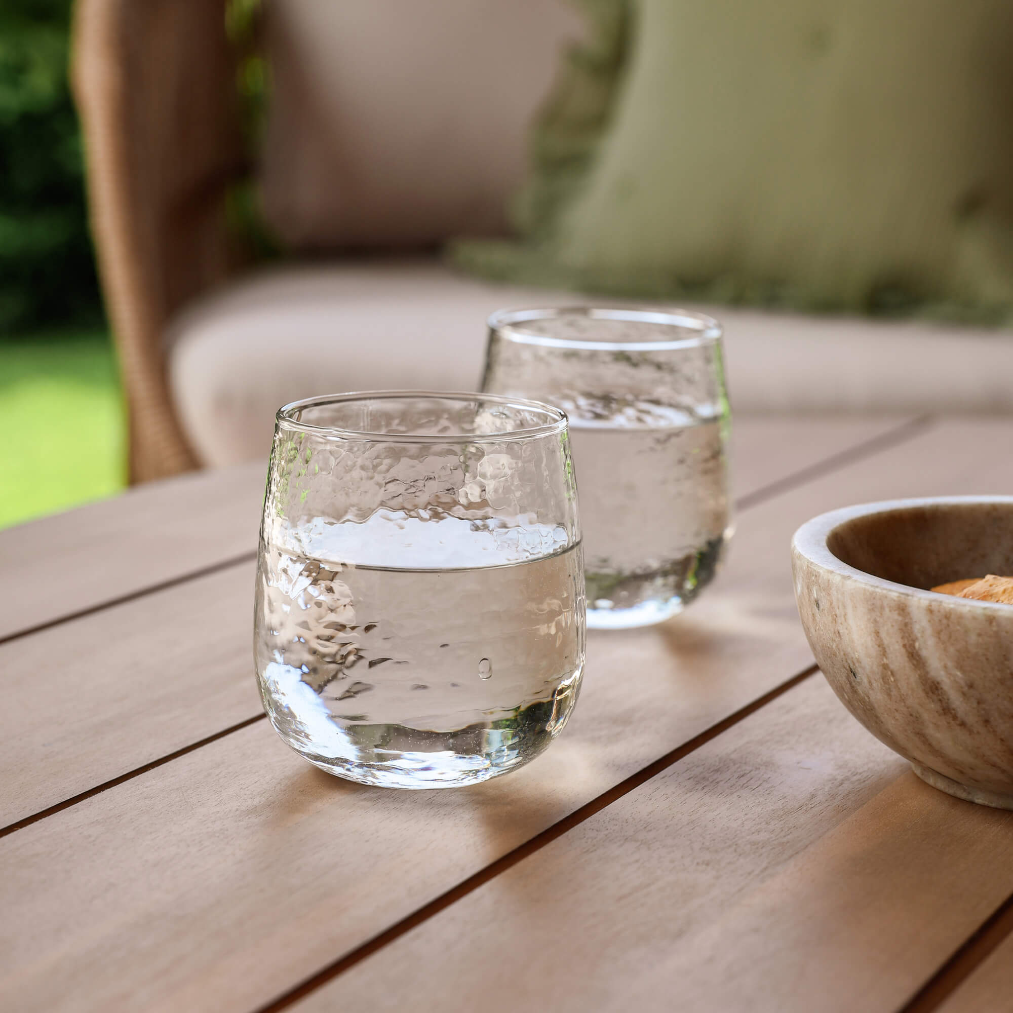 Due bicchieri trasparenti d'acqua su un tavolo di legno in giardino accanto a una ciotola di pietra