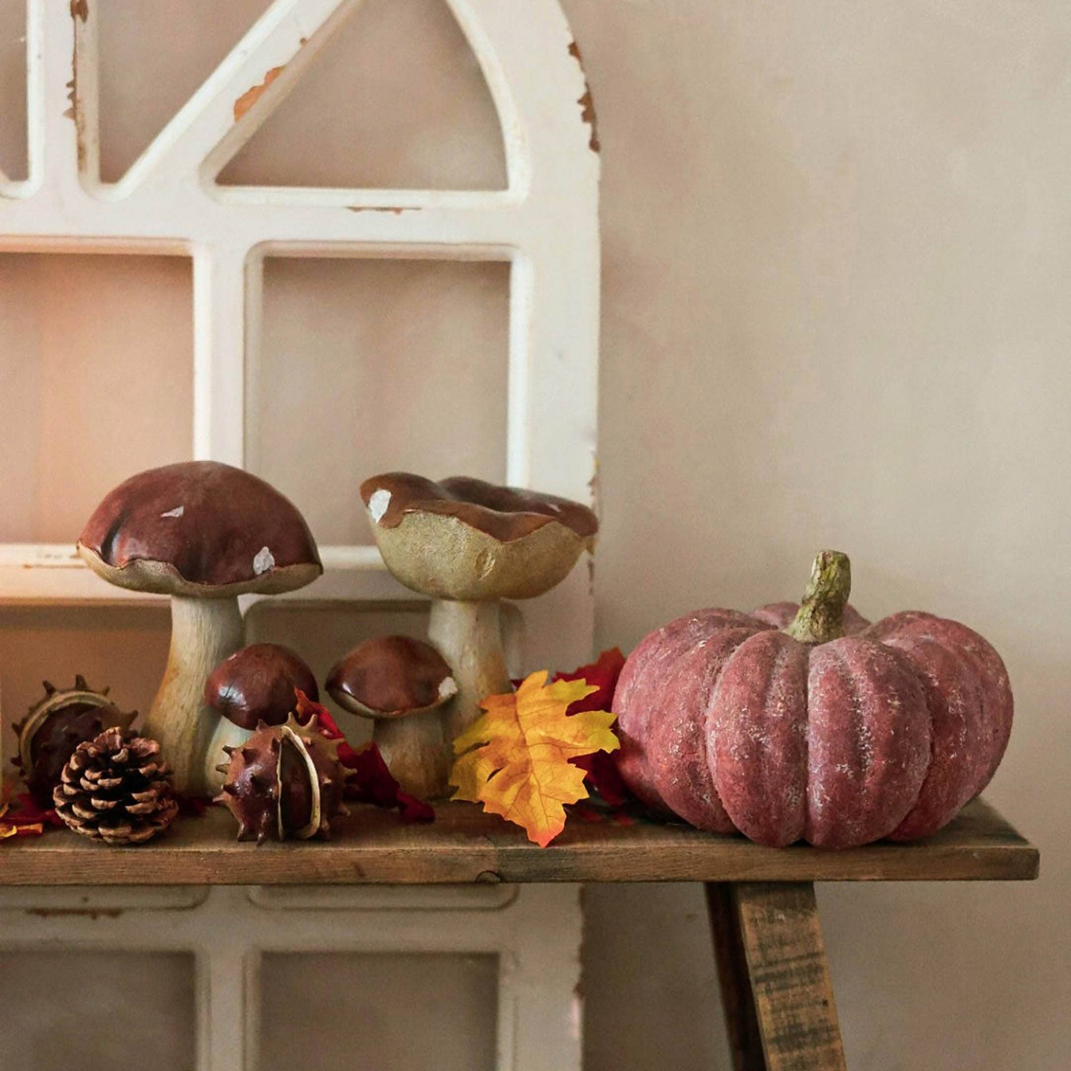 Decorazione autunnale con funghi in ceramica e zucca rosa su mensola in legno rustico