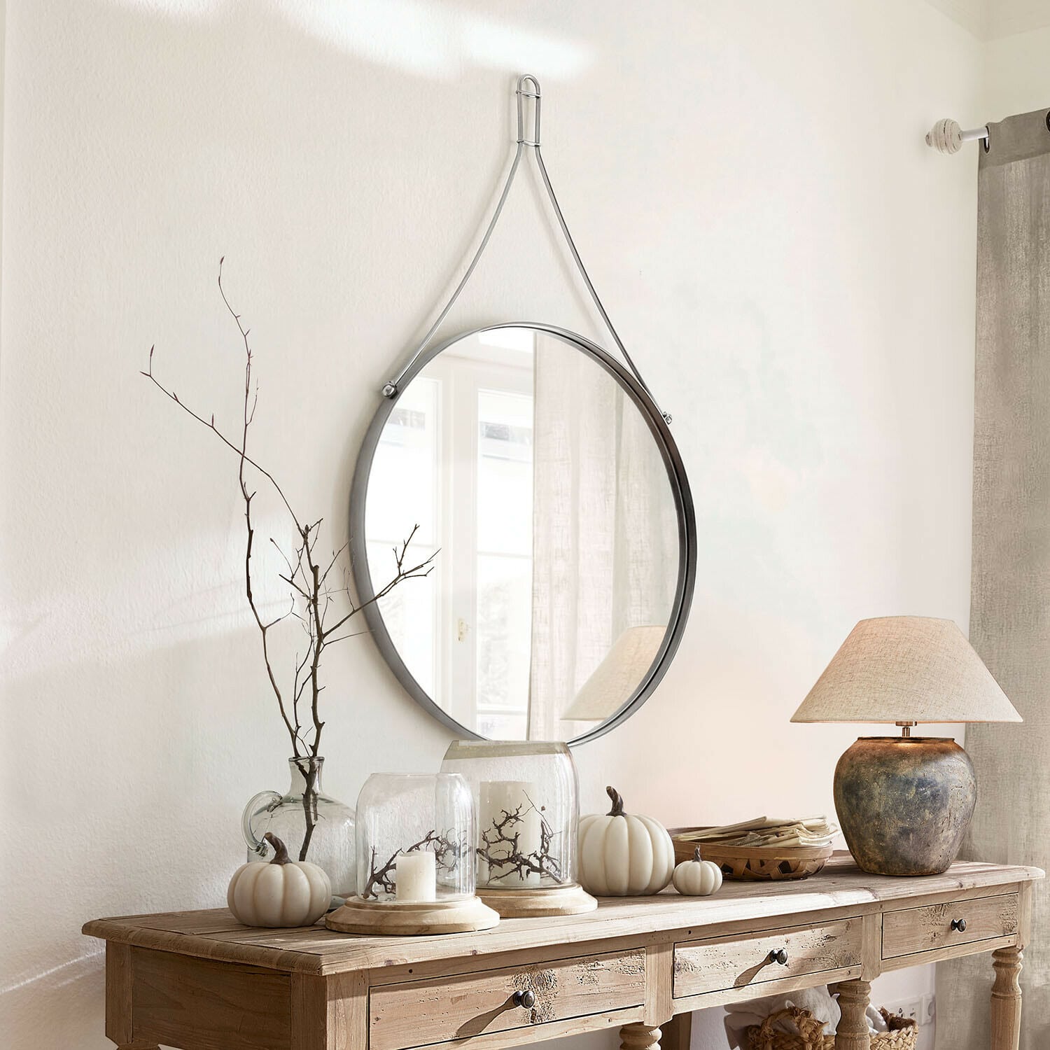 Specchio Célivaux Specchio rotondo appeso con cinghia metallica argento sopra consolle in legno con decorazioni