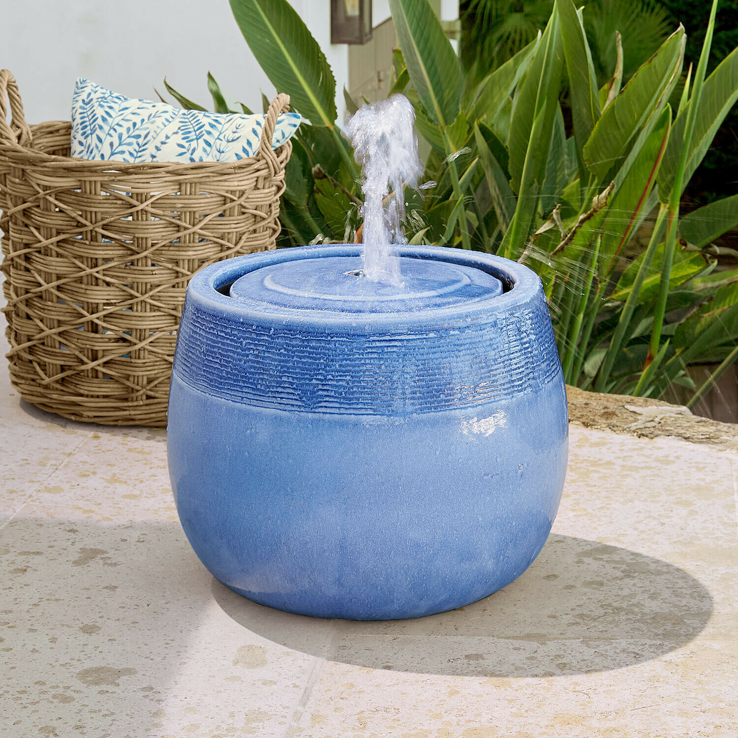Fontana Seravia Fontana da giardino in ceramica blu con getto d'acqua, circondata da piante verdi e cesta in vimini