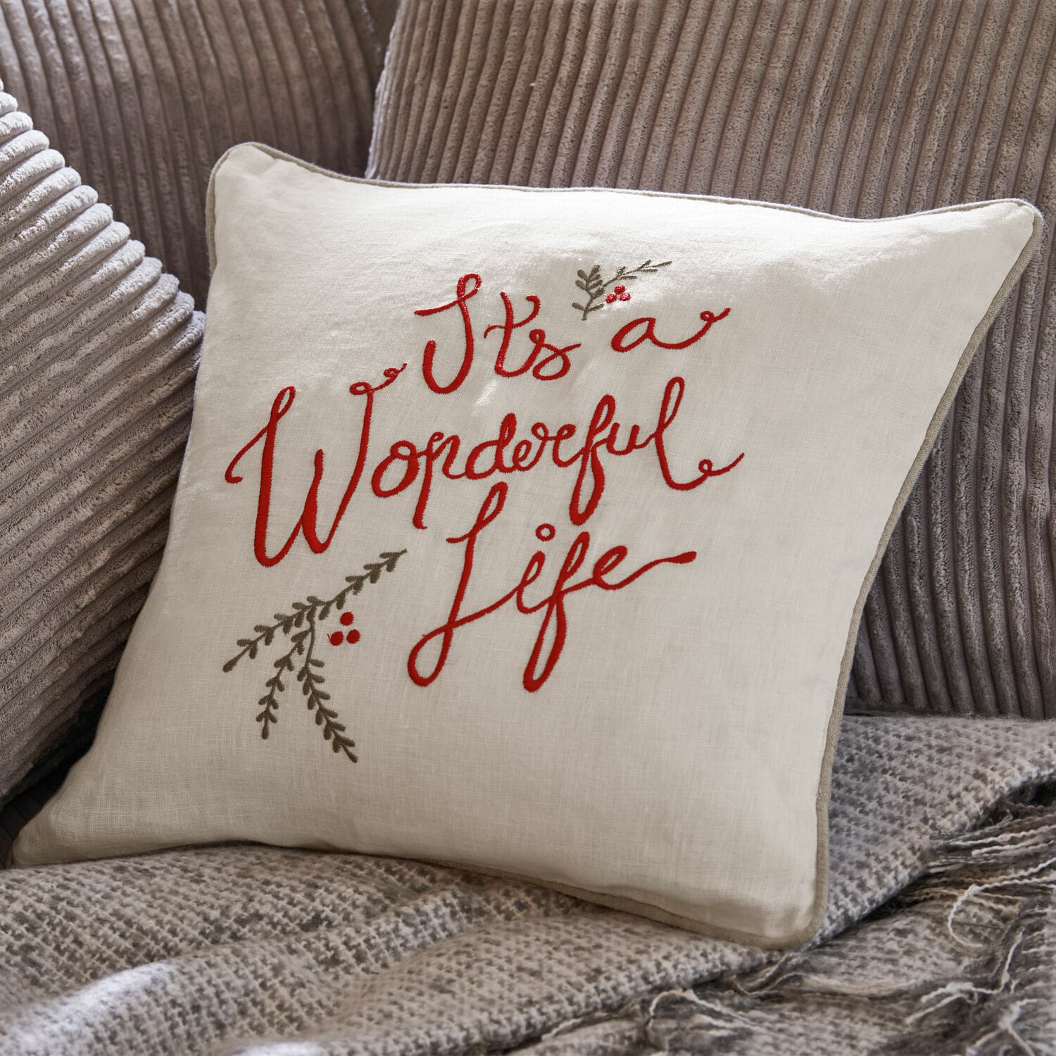 Copricuscino Wonderful Cuscino beige in lino con ricamo rosso "It's a Wonderful Life" su tessuto grigio.