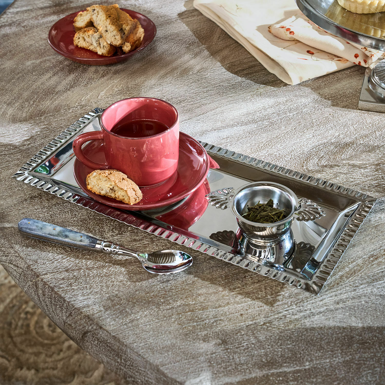 Set da tè Arivelle Vassoio rettangolare in metallo argentato con tazza rossa, tè e biscotto su tavolo in legno