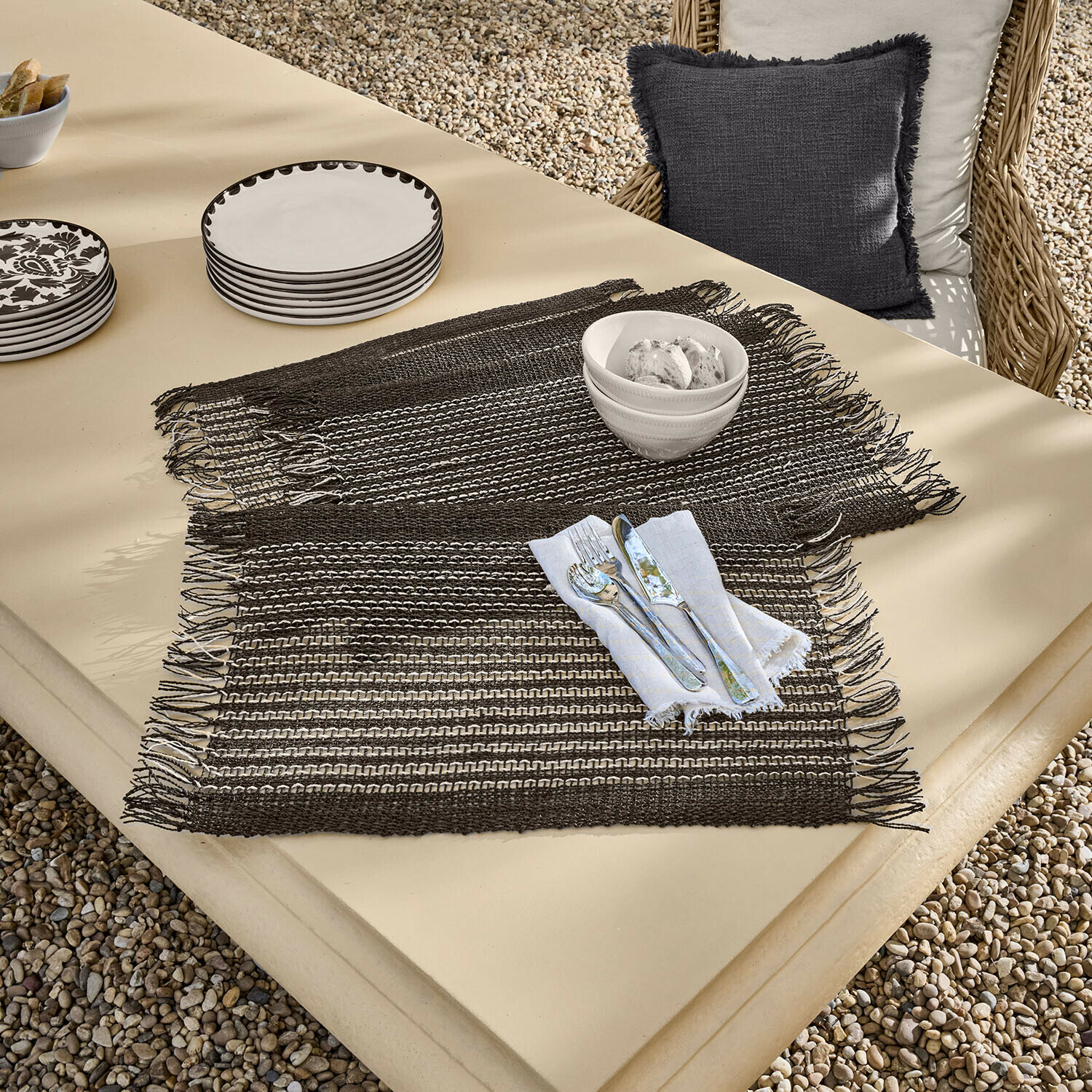 Set di 4 tovagliette Tarevo Tovagliette intrecciate marroni con frange su tavolo beige con stoviglie e posate