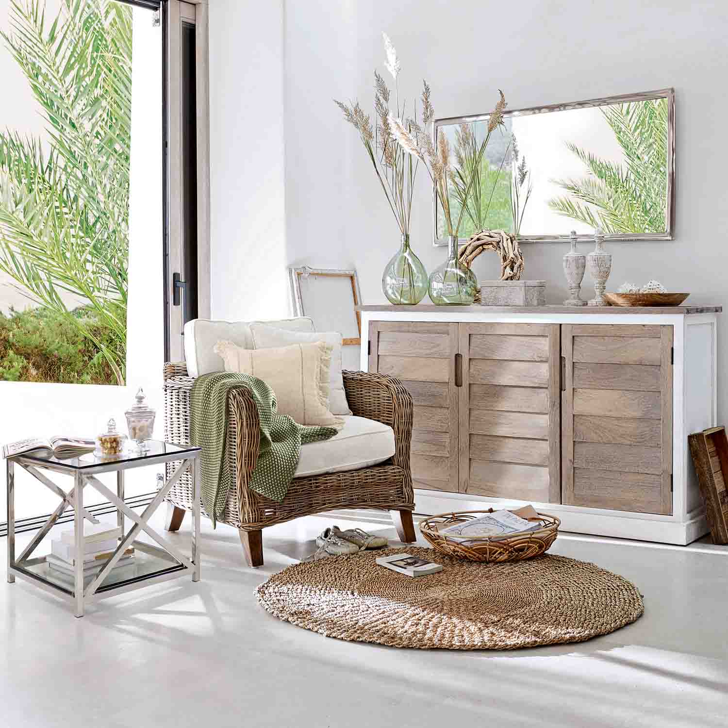 Soggiorno luminoso con poltrona in vimini, credenza in legno chiaro e tappeto rotondo naturale per un ambiente accogliente