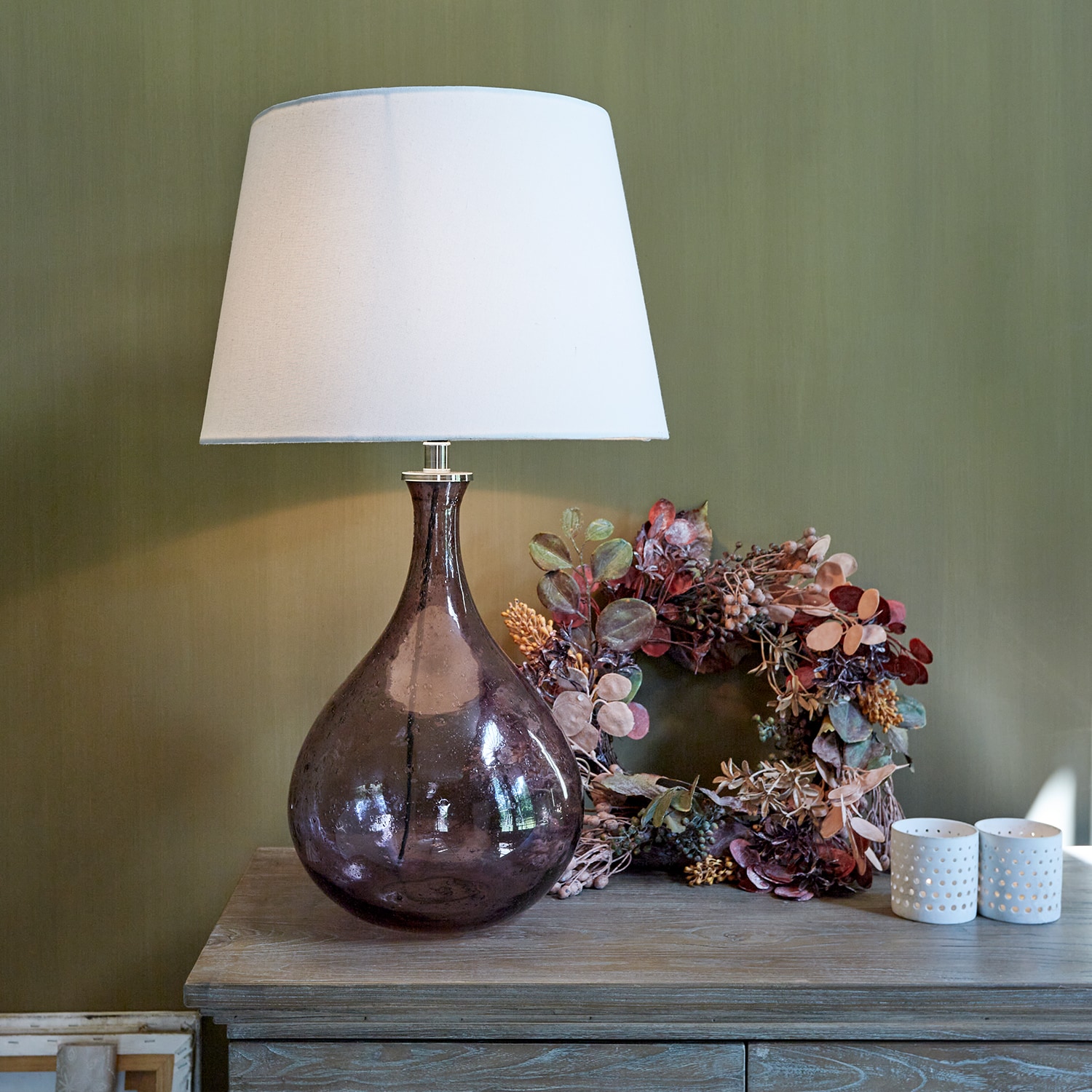 Lampada da tavolo in vetro con paralume bianco e base marrone trasparente su tavolo in legno con decorazioni