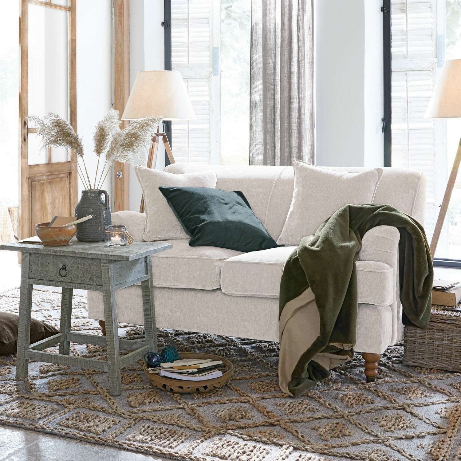 Divano beige in tessuto morbido con coperta verde e cuscino in soggiorno accogliente con tavolino in legno