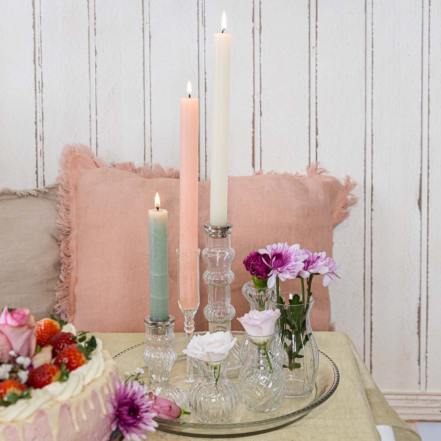 Set di candele pastello e piccoli vasi di vetro con fiori su un vassoio di vetro sul tavolo