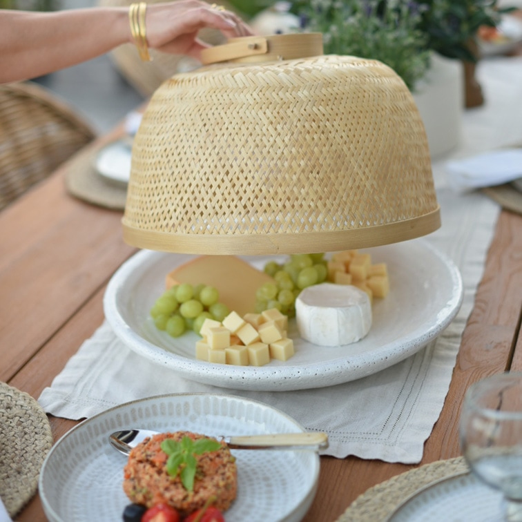 Copertura in bambù naturale protegge formaggi e uva verde su piatto bianco su tavolo in legno