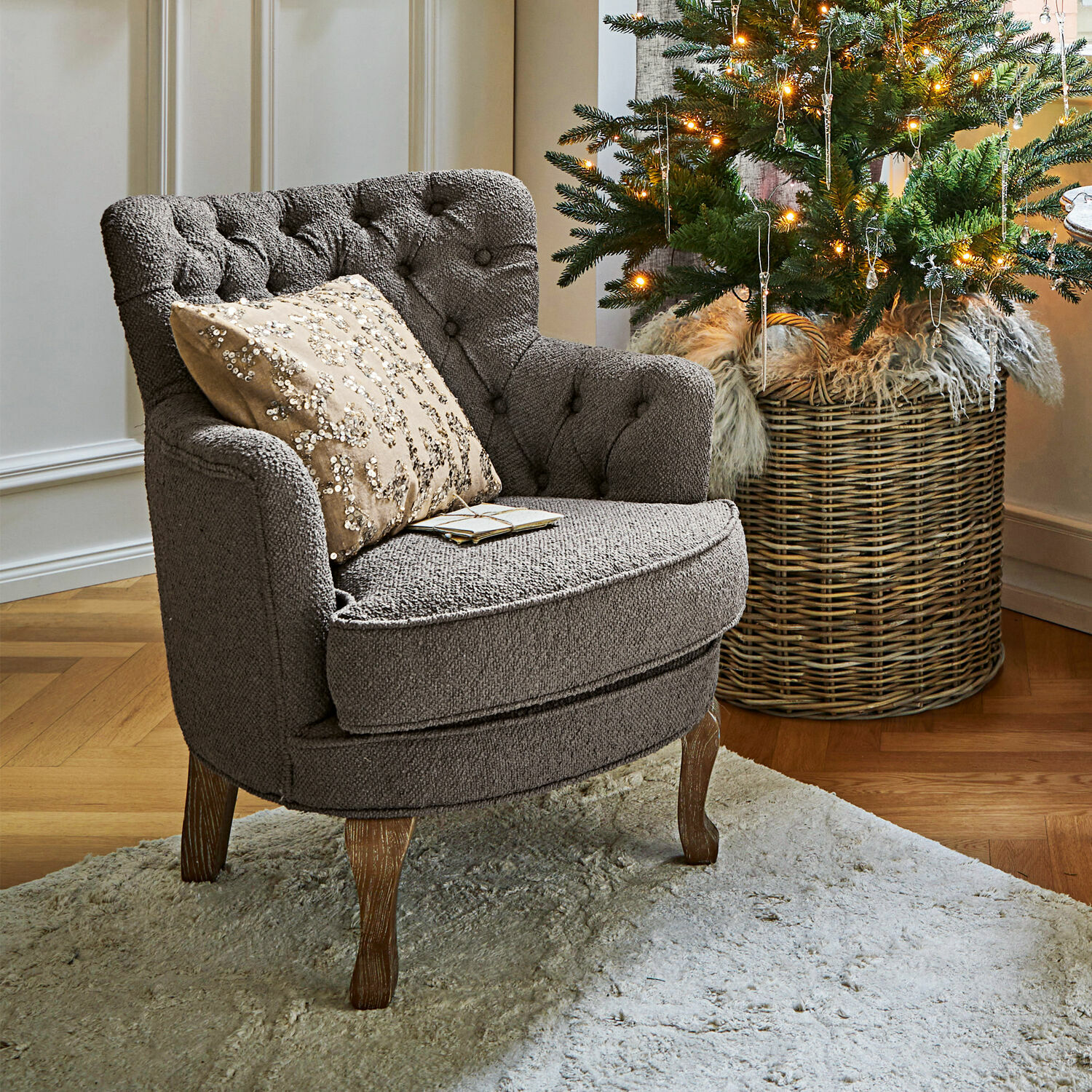 Poltrona Calgary Poltrona grigia imbottita con gambe in legno su tappeto chiaro accanto ad albero di Natale decorato