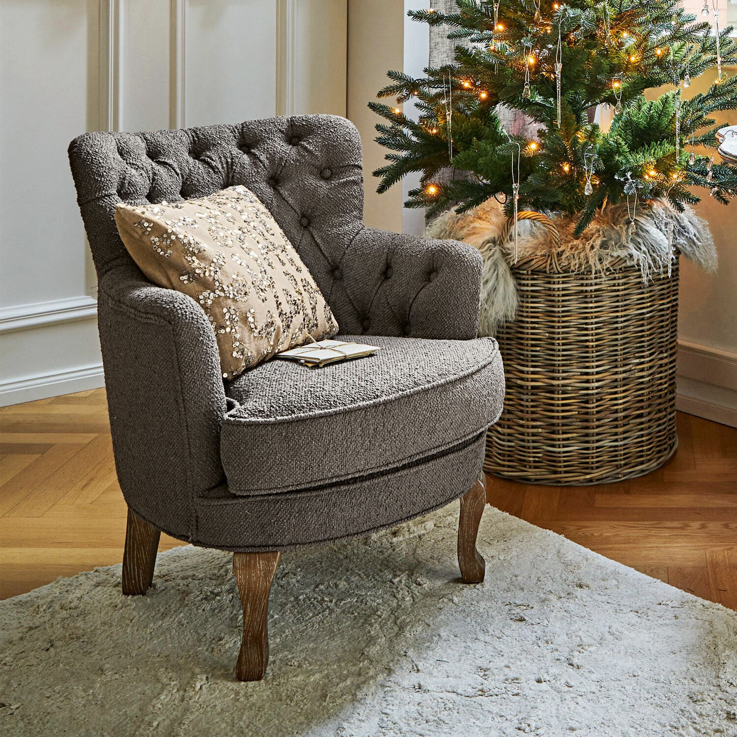 Poltrona Calgary Poltrona grigia imbottita con gambe in legno su tappeto chiaro accanto ad albero di Natale decorato