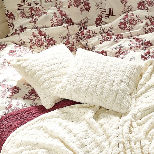 Cuscini e coperta in peluche crema su letto con copripiumino a fiori bordeaux