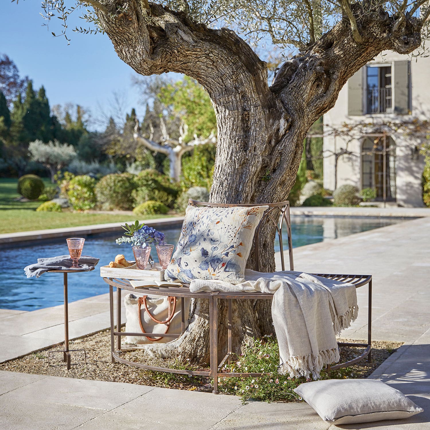 Panchina in metallo intorno a un albero con cuscino e coperta vicino a una piscina in giardino