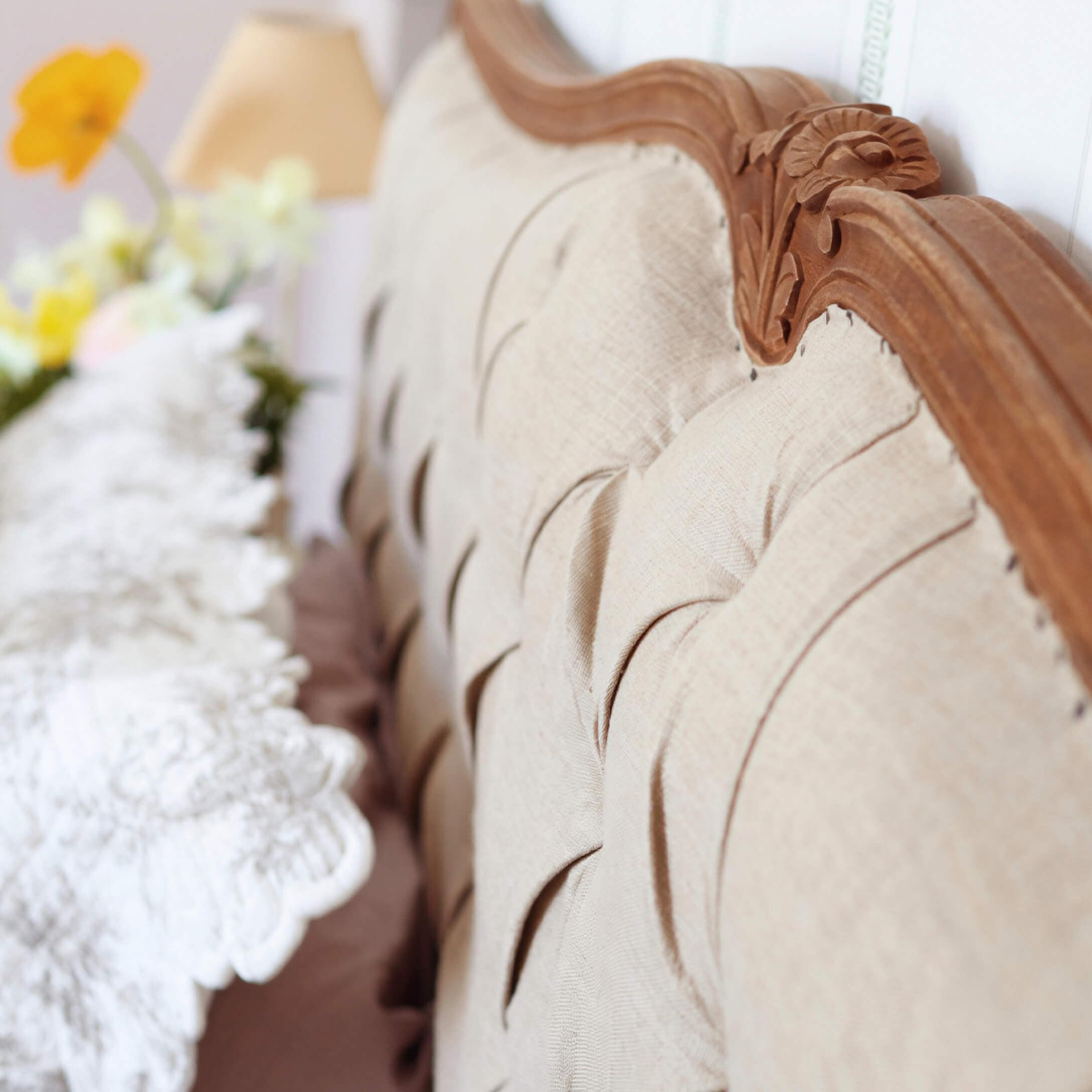 Schienale imbottito beige con cornice in legno intagliato e cuscino decorativo sfocato sullo sfondo