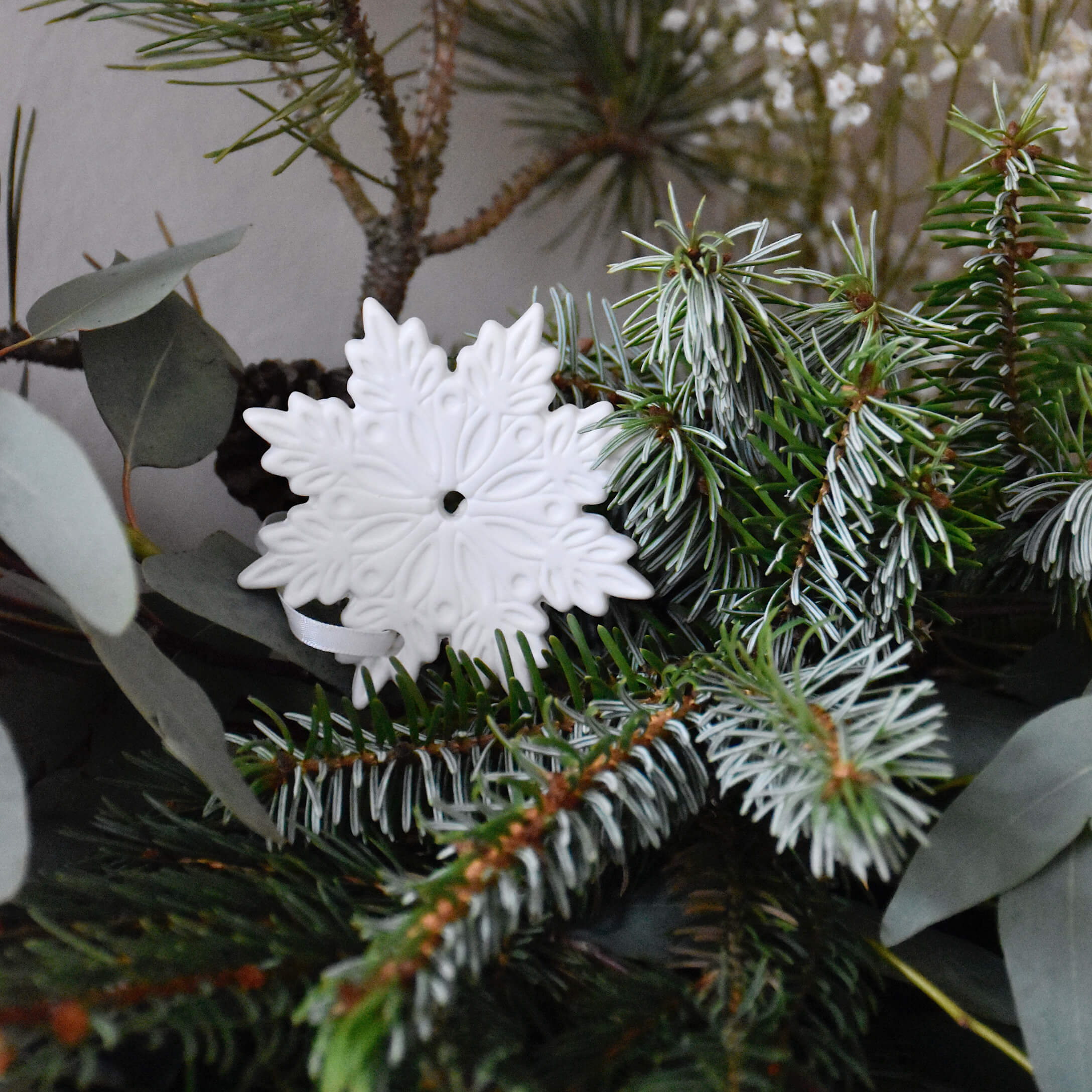 Decorazione natalizia in ceramica bianca a forma di fiocco di neve su rami verdi di abete