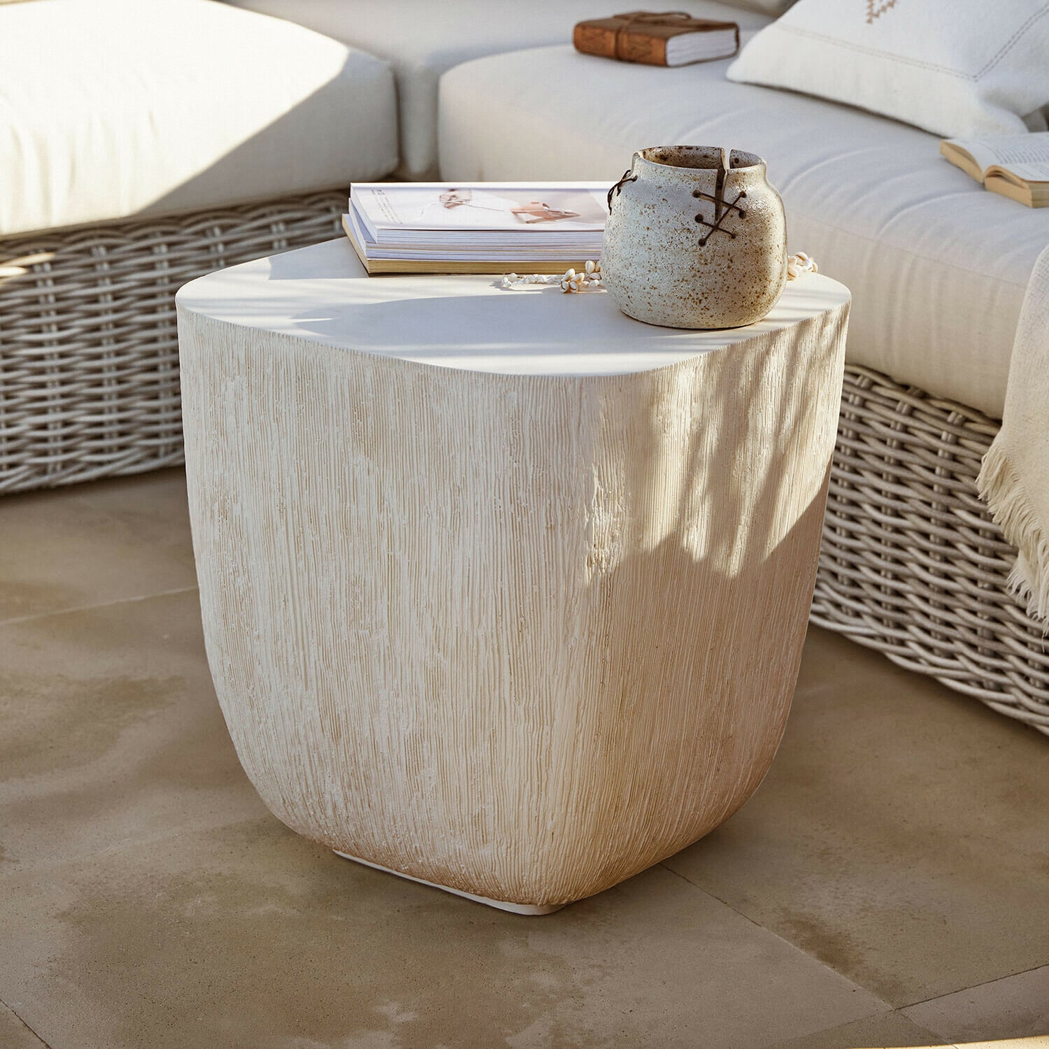 Tavolino Nélomiane Tavolino beige con texture legno, vaso in ceramica e libri su terrazza con divano in rattan