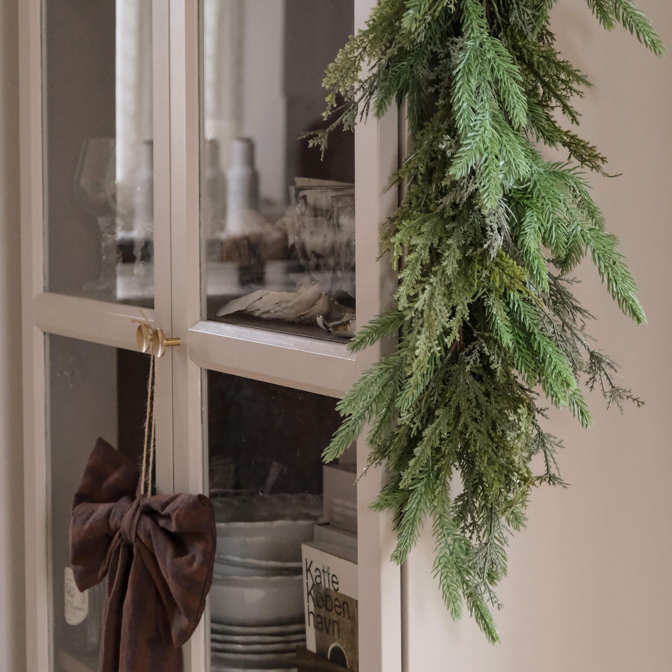 Ghirlanda decorativa verde di rami appesa a un armadio chiaro con porte in vetro stile scandinavo