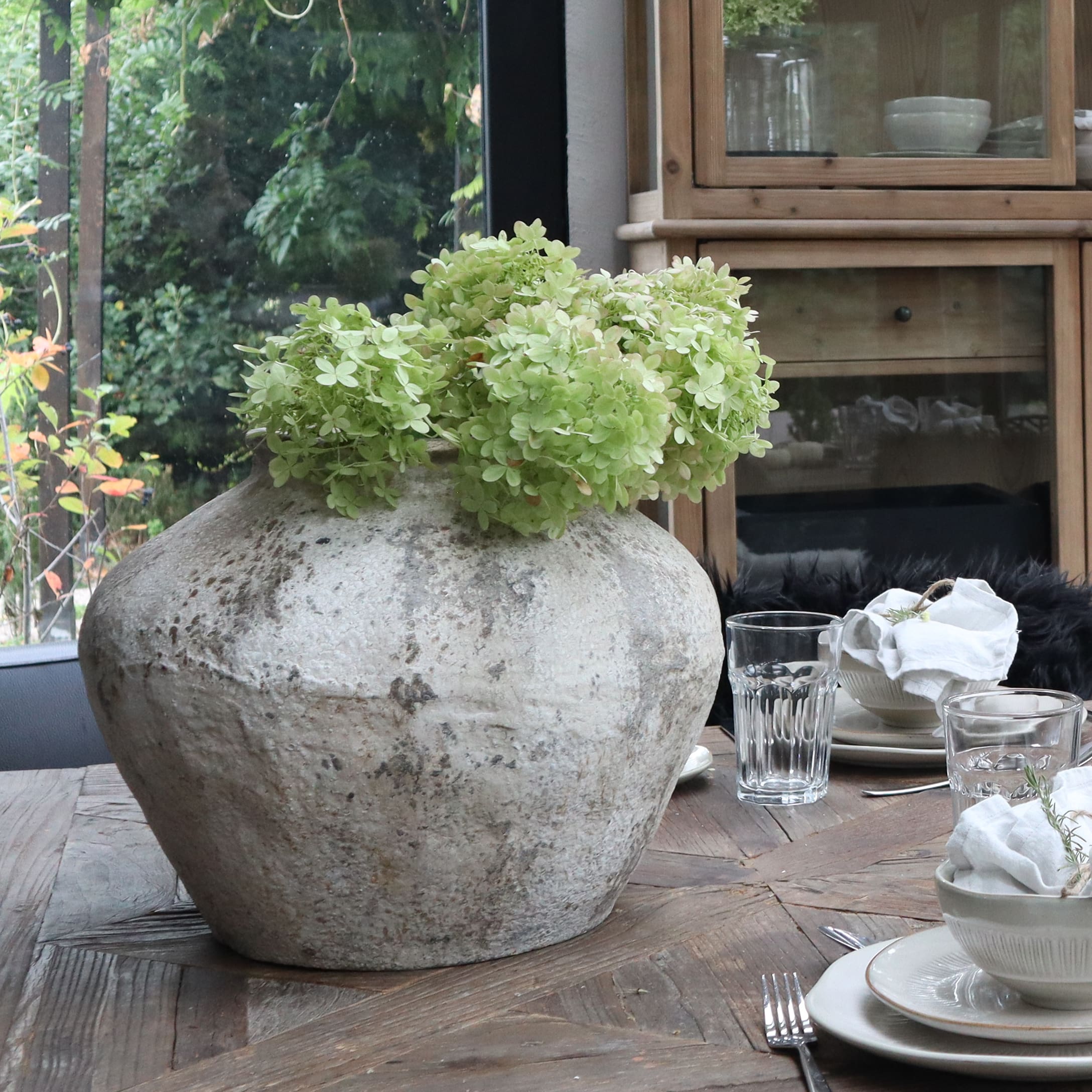 Grande vaso in ceramica grigia con fiori verdi su tavolo in legno in sala da pranzo