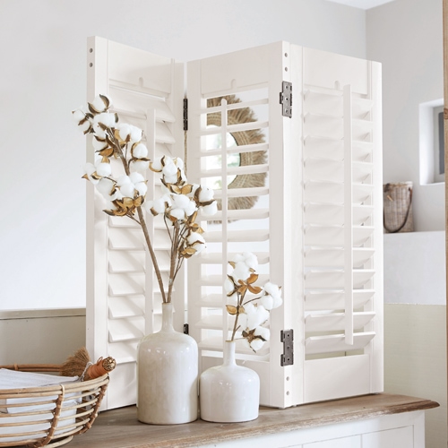 Paravento in legno bianco con persiane su tavolo, decorato con fiori di cotone, stile rustico
