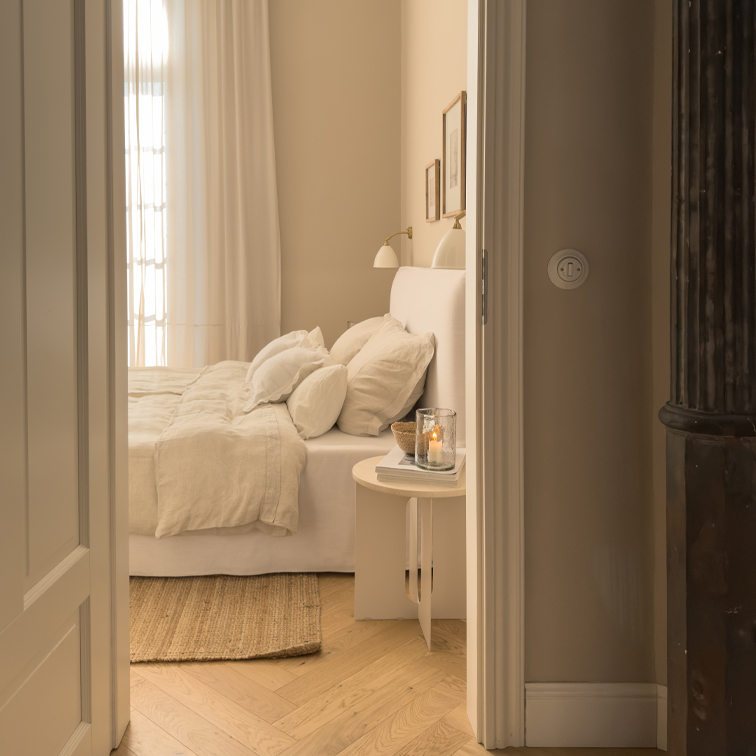Camera da letto accogliente in tonalità beige chiaro con letto e tappeto naturale su pavimento in legno chiaro