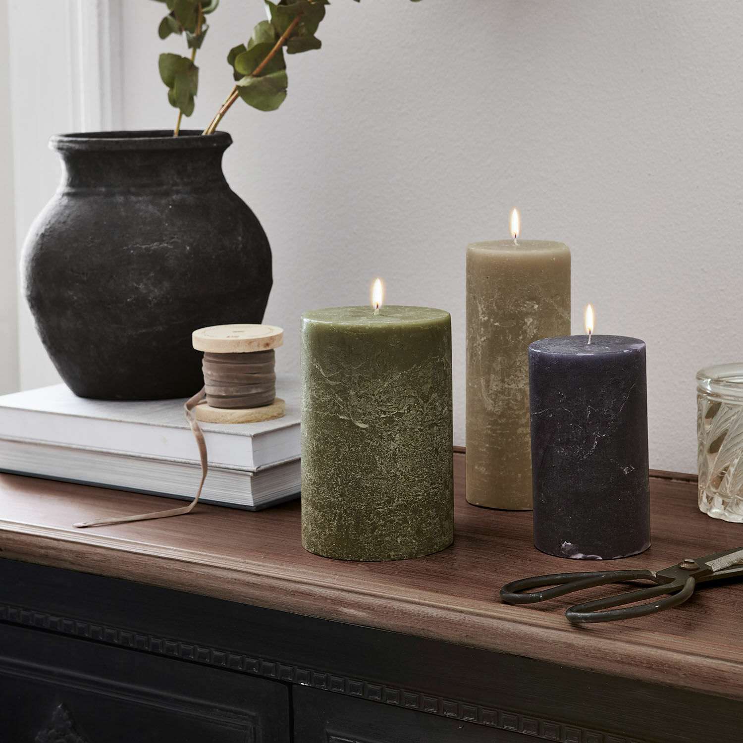 Set di 3 candele Pretin Tre candele accese verde, beige e nero su piano in legno con decorazioni