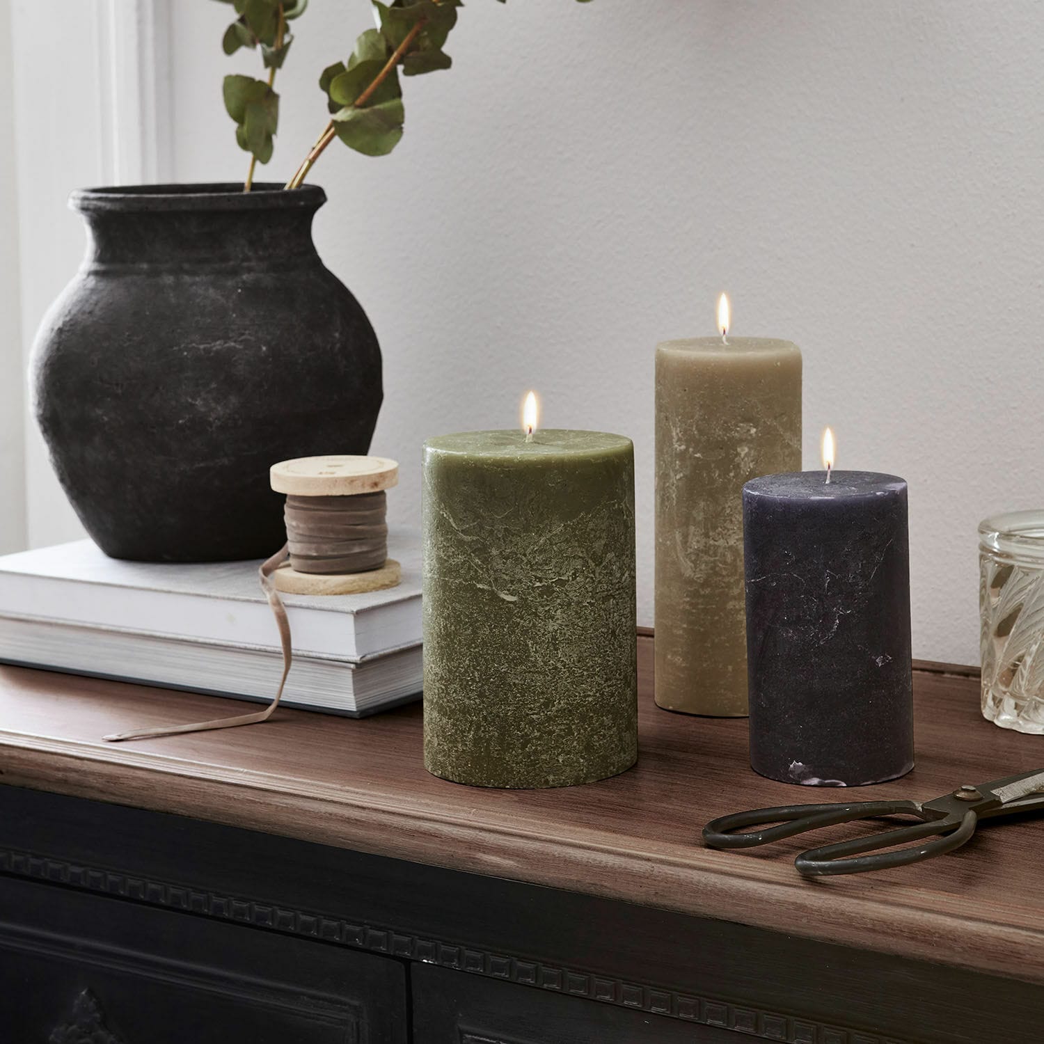 Set di 3 candele Pretin Tre candele accese verde, beige e nero su piano in legno con decorazioni