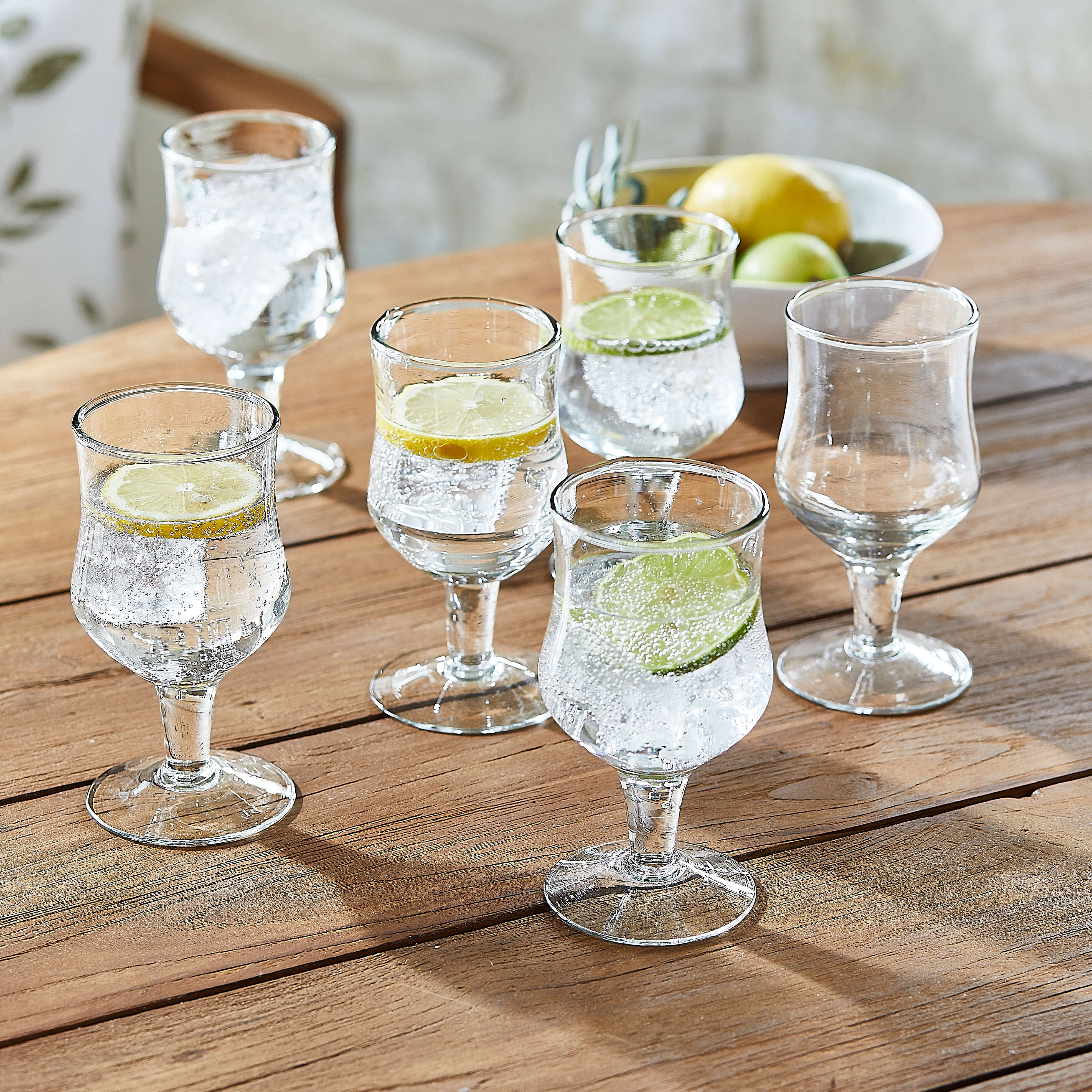 Set di sei bicchieri trasparenti con acqua e fette di limone e lime su tavolo in legno
