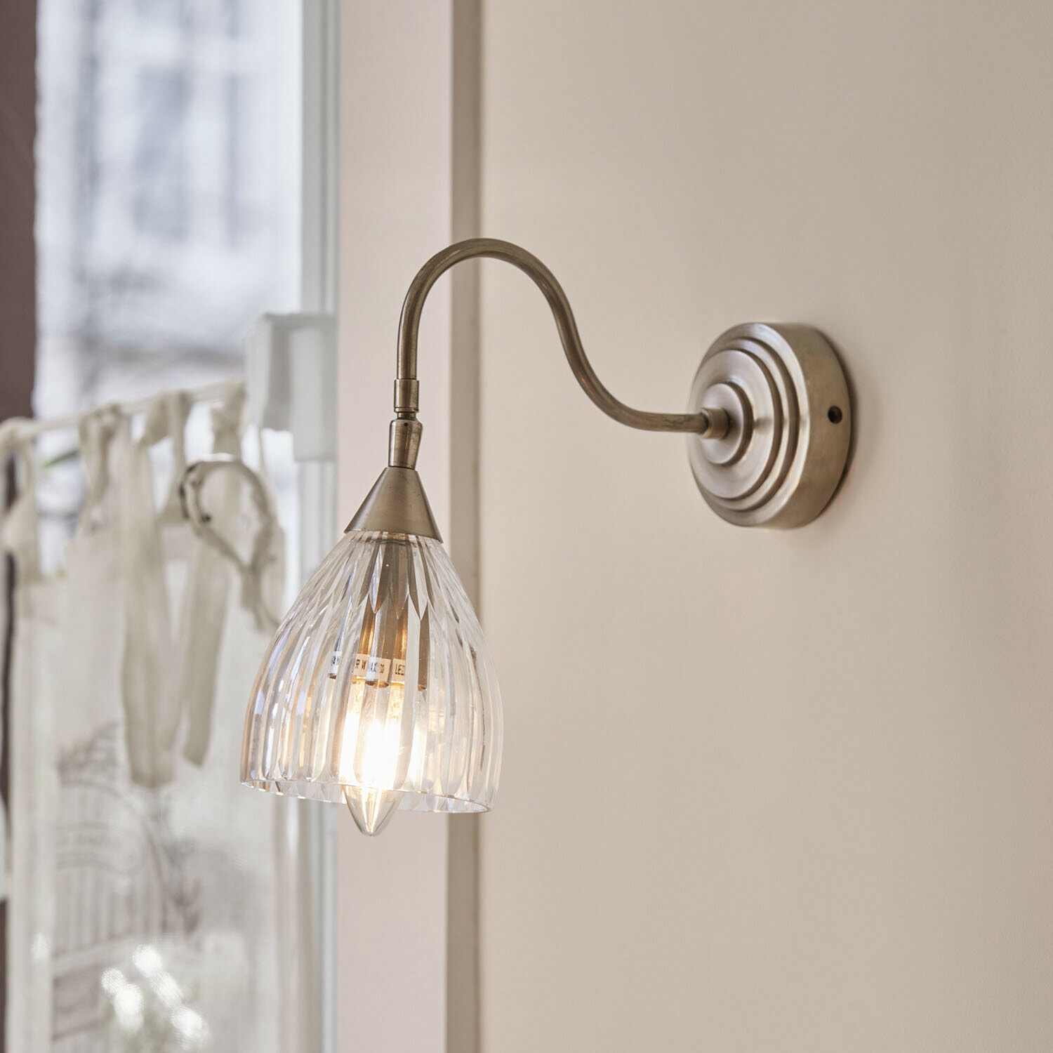 Lampada da parete Niamhs Applique da parete con paralume in vetro trasparente e braccio in metallo color argento antico