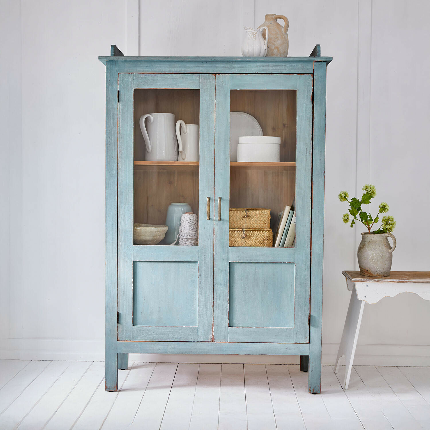Vetrina Nouvellese Mobile in legno blu con ante in vetro e decorazioni in ceramica vintage in stanza luminosa