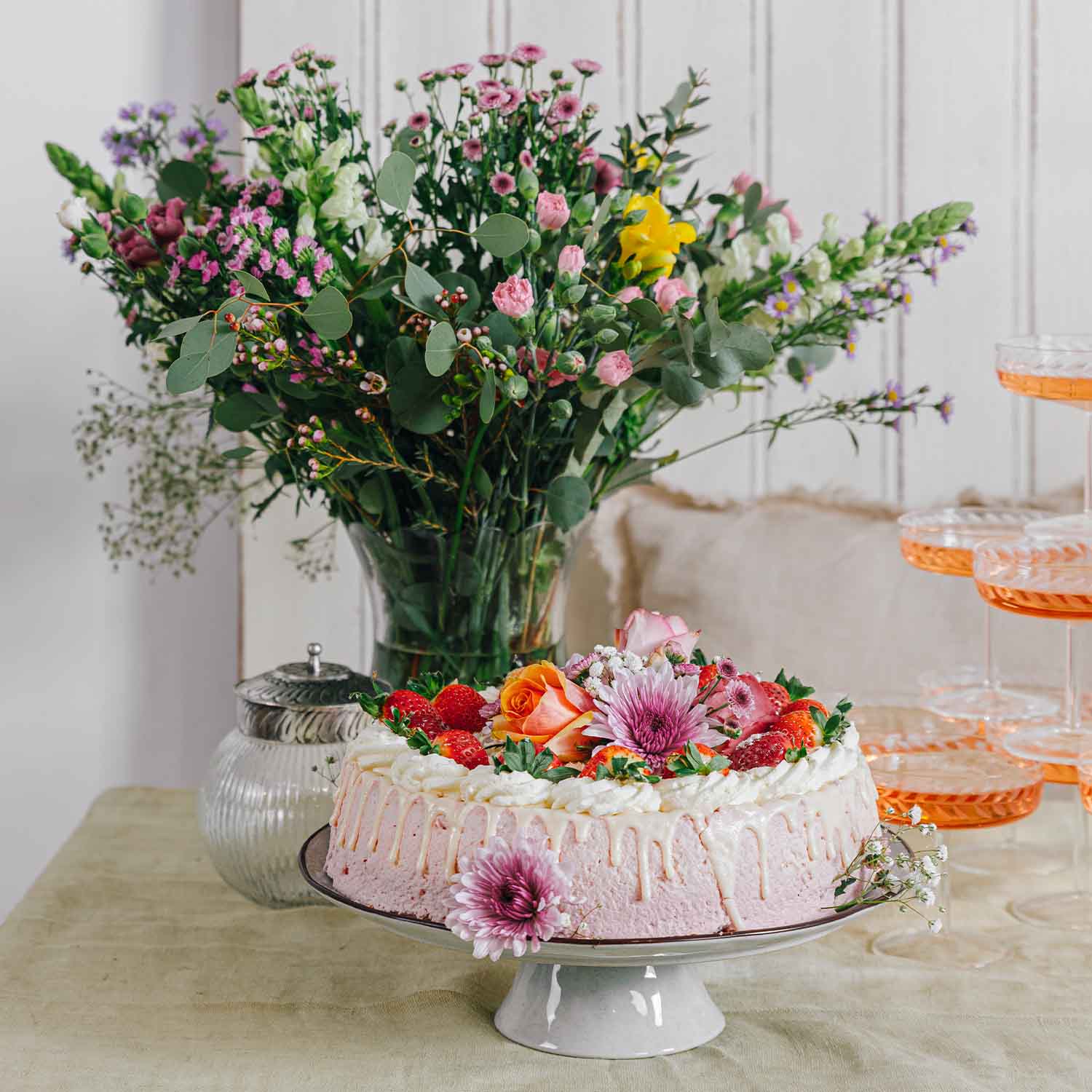 Torta rosa con crema, fragole fresche e fiori decorativi su alzata bianca con bouquet sullo sfondo