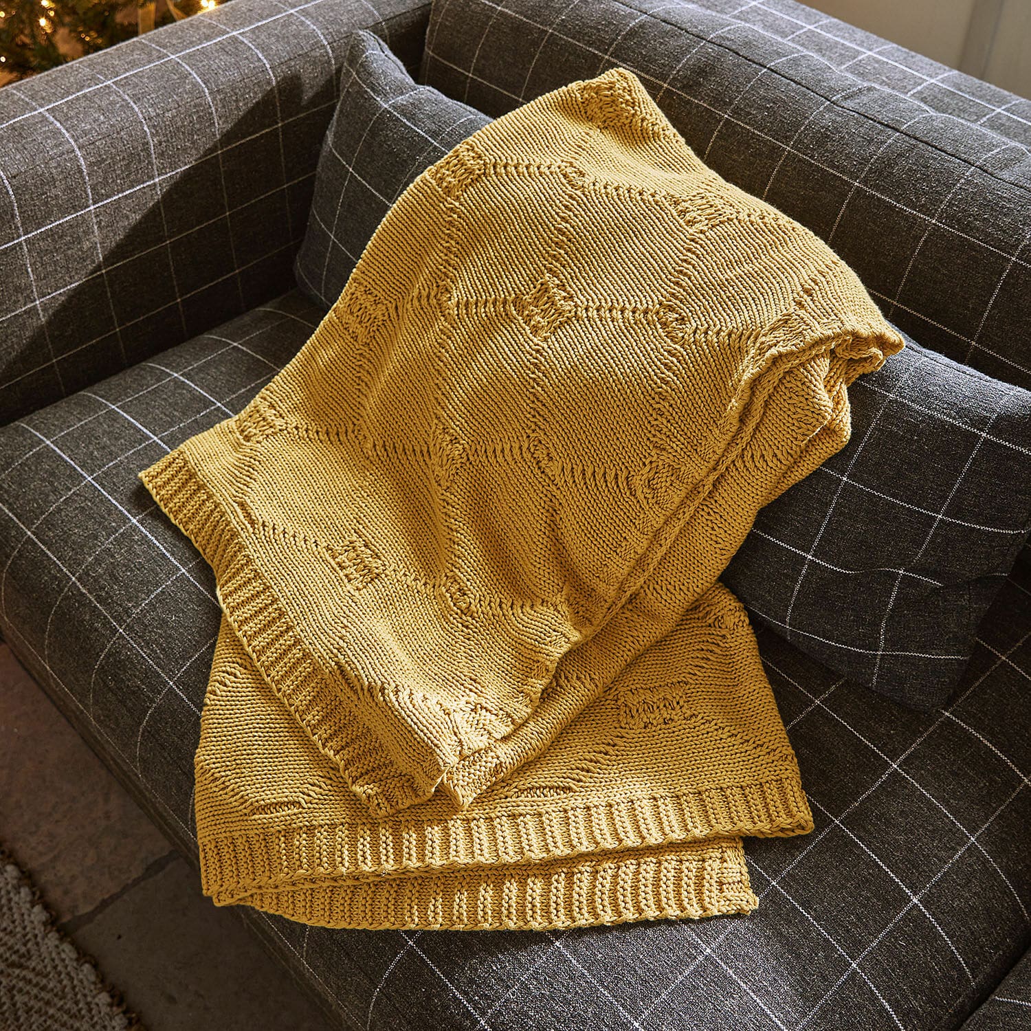 Coperta Cresil Coperta gialla lavorata a maglia con motivo geometrico su divano grigio a quadri