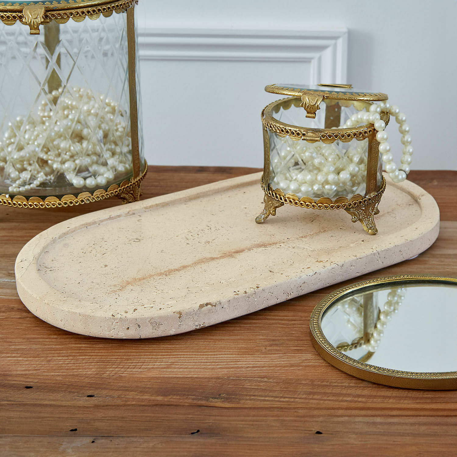 Ciotola Thalina Scatola di vetro con cornice in ottone e perle su vassoio in pietra beige su tavolo in legno