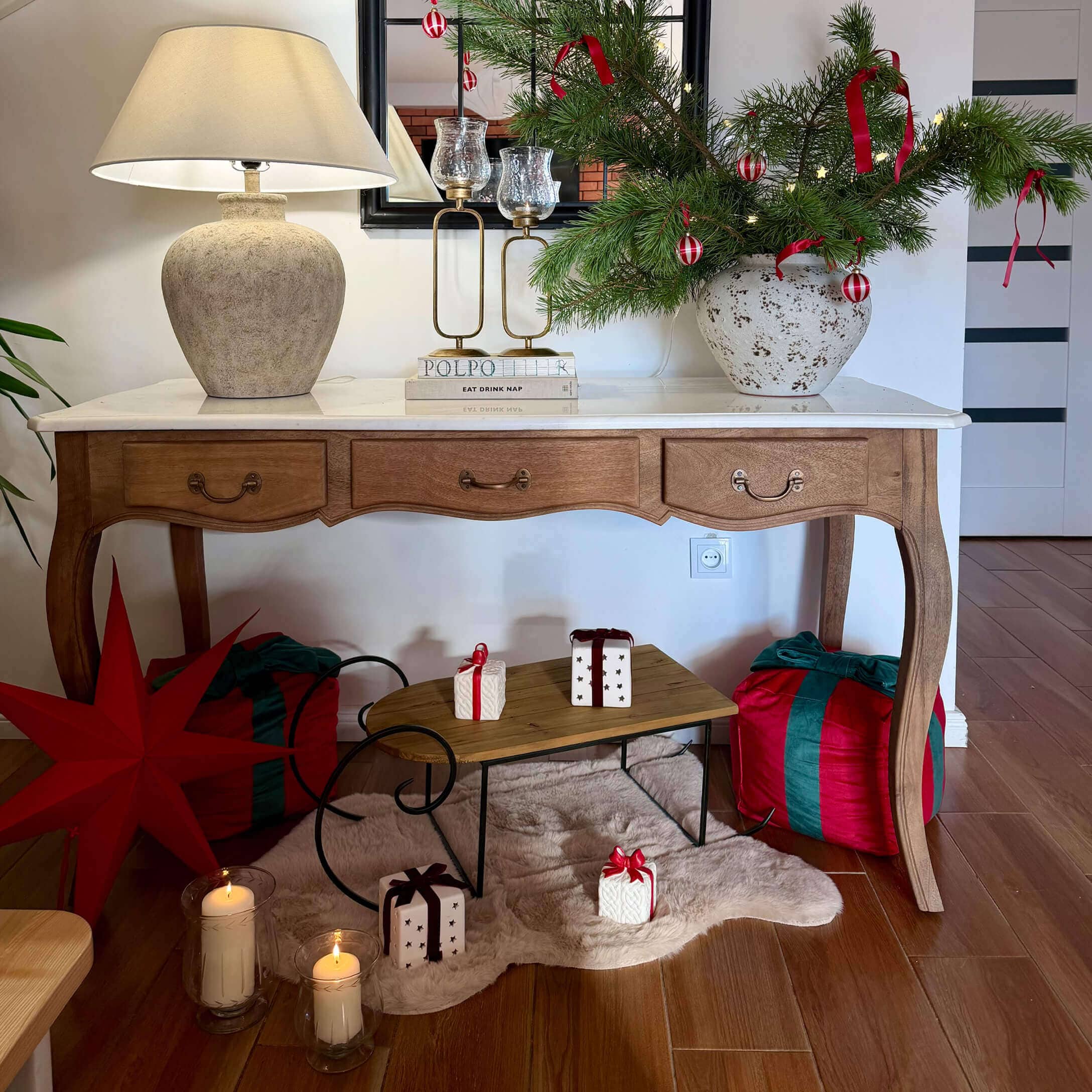 Tavolo in legno con piano bianco, lampada e decorazioni natalizie con rami verdi e nastri rossi
