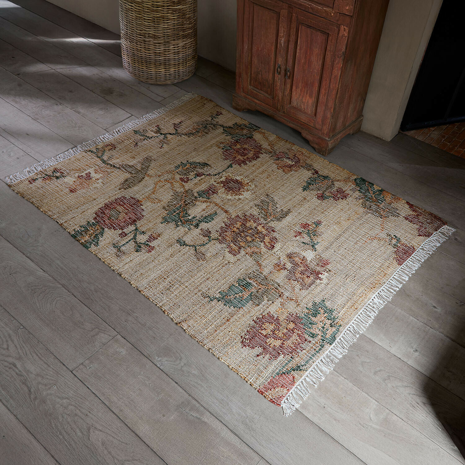 Tappeto Caléndoro Tappeto beige in materiale naturale con motivo floreale e frange su pavimento in legno chiaro